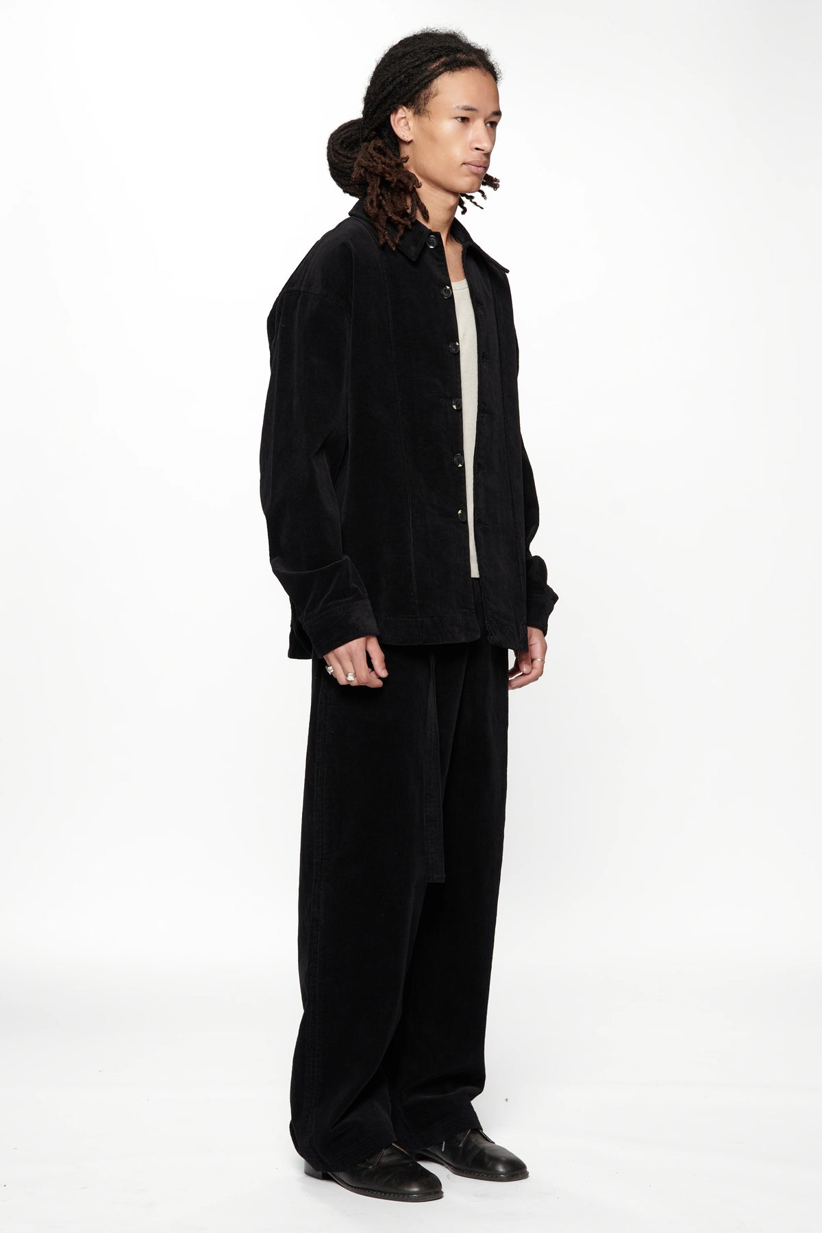 Side view of a person wearing a Vintage Black Corduroy Float Overshirt with black pants and shoes on a white background