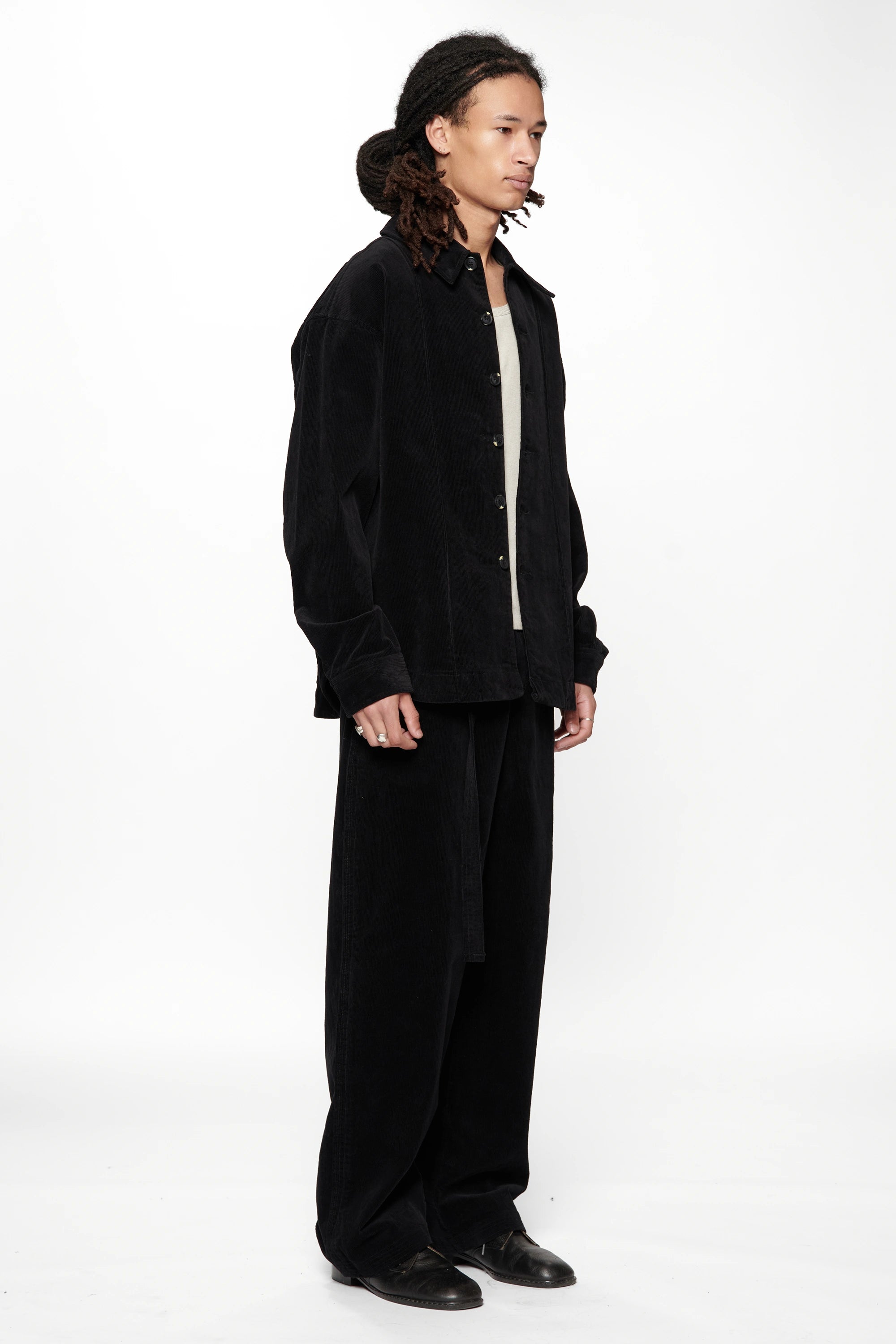 Side view of a person wearing a Vintage Black Corduroy Float Overshirt with black pants and shoes on a white background