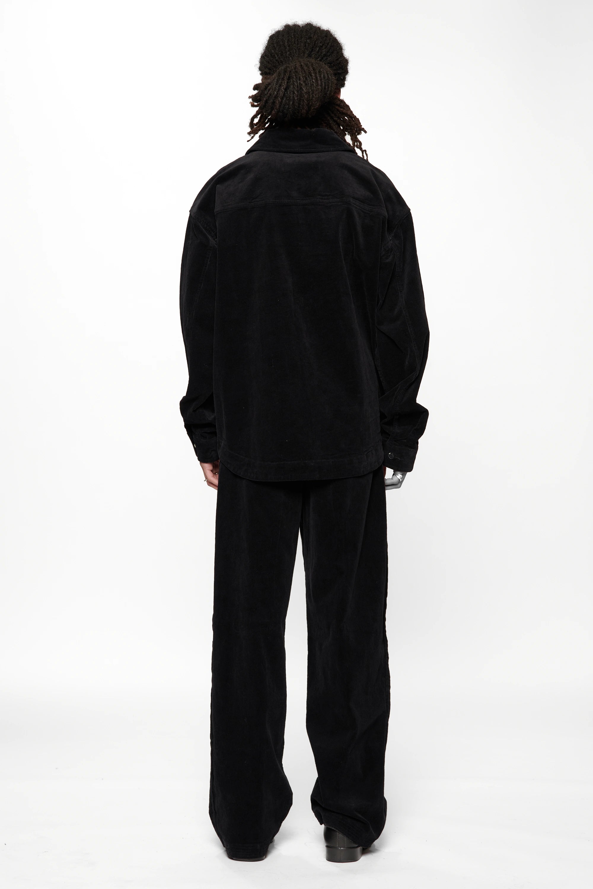 View from the back of a person wearing a Vintage Black Corduroy Float Overshirt with black pants and shoes on a white background