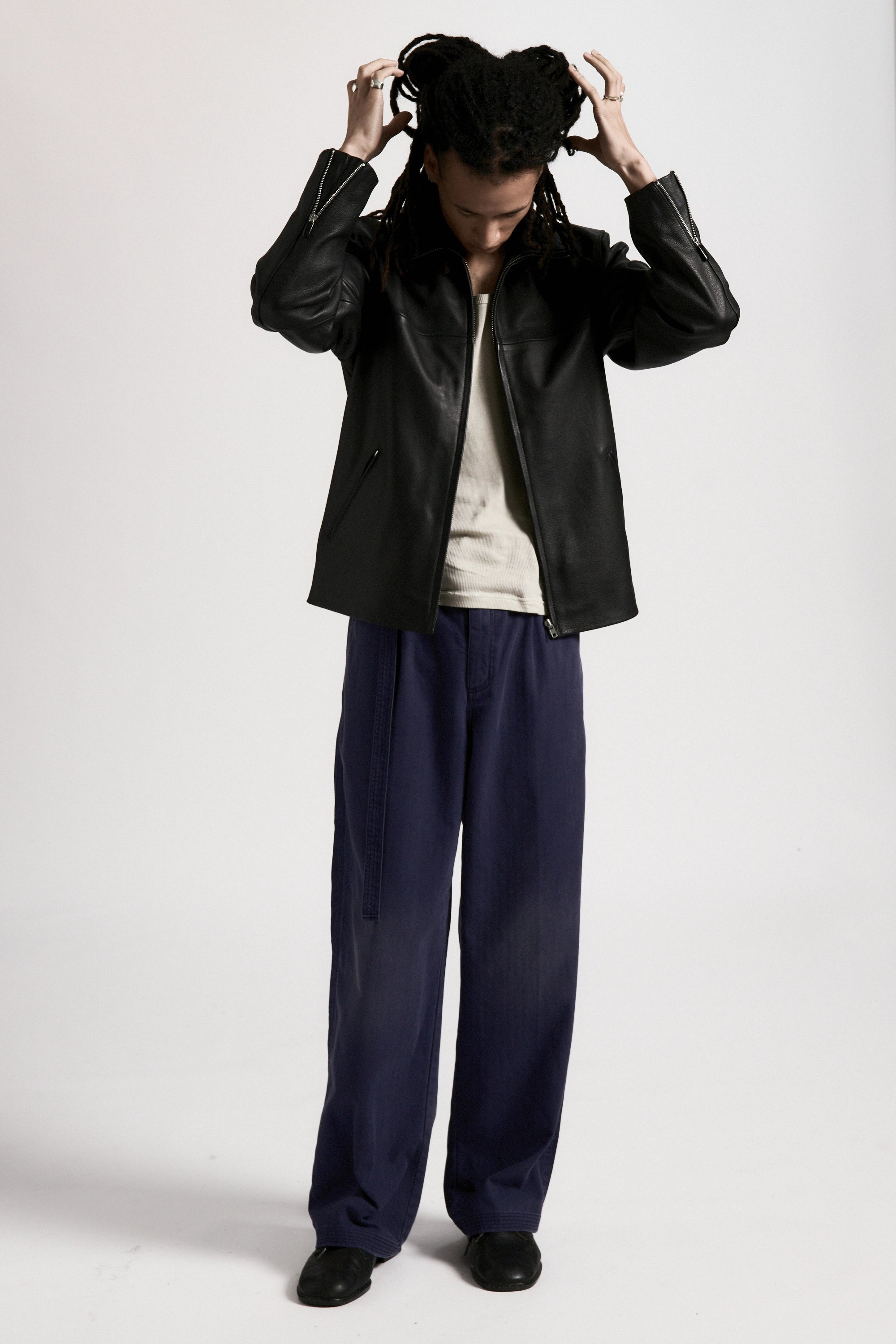 Person wearing the men's Bank Jacket, a black leather jacket made from full grain leather, and dark pants on a white background