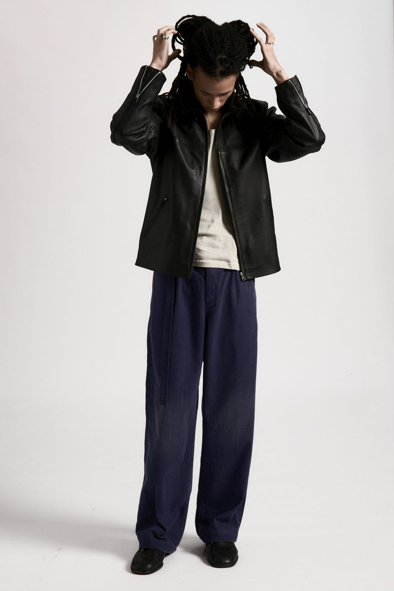 Person wearing the men's Bank Jacket, a black leather jacket made from full grain leather, and dark pants on a white background
