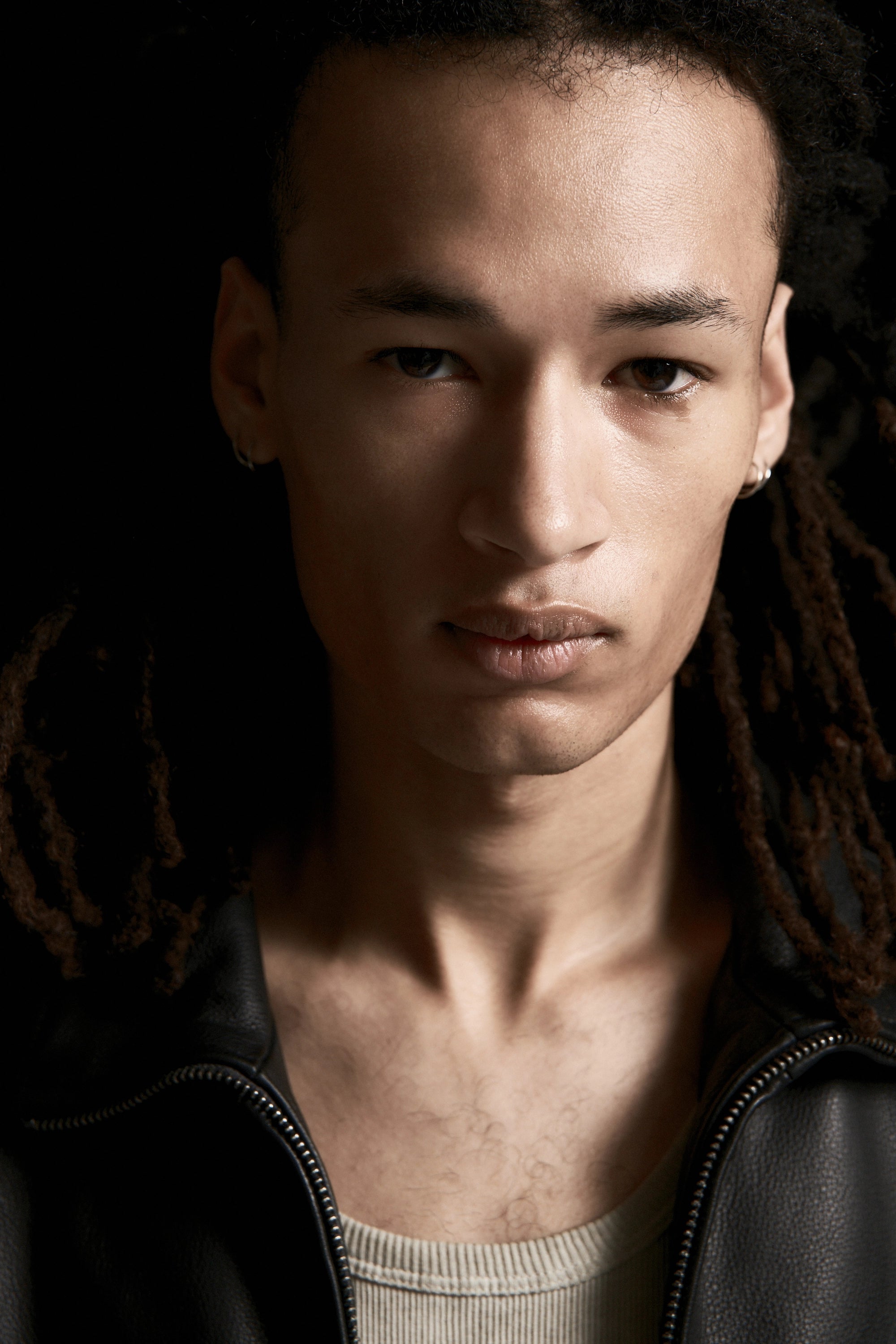 Close up view of a person with dreadlocks wearing a black jacket against a dark background