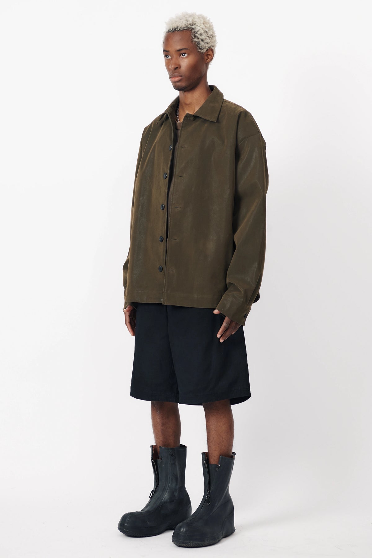 A person standing facing off to the side wearing the Beach Brains black baggy shorts an oversized green shirt with front pleats.