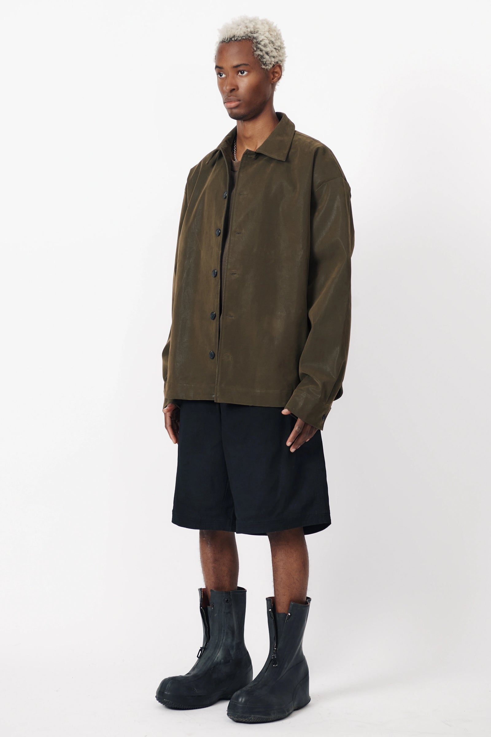 A person standing facing off to the side wearing the Beach Brains black baggy shorts an oversized green shirt with front pleats.
