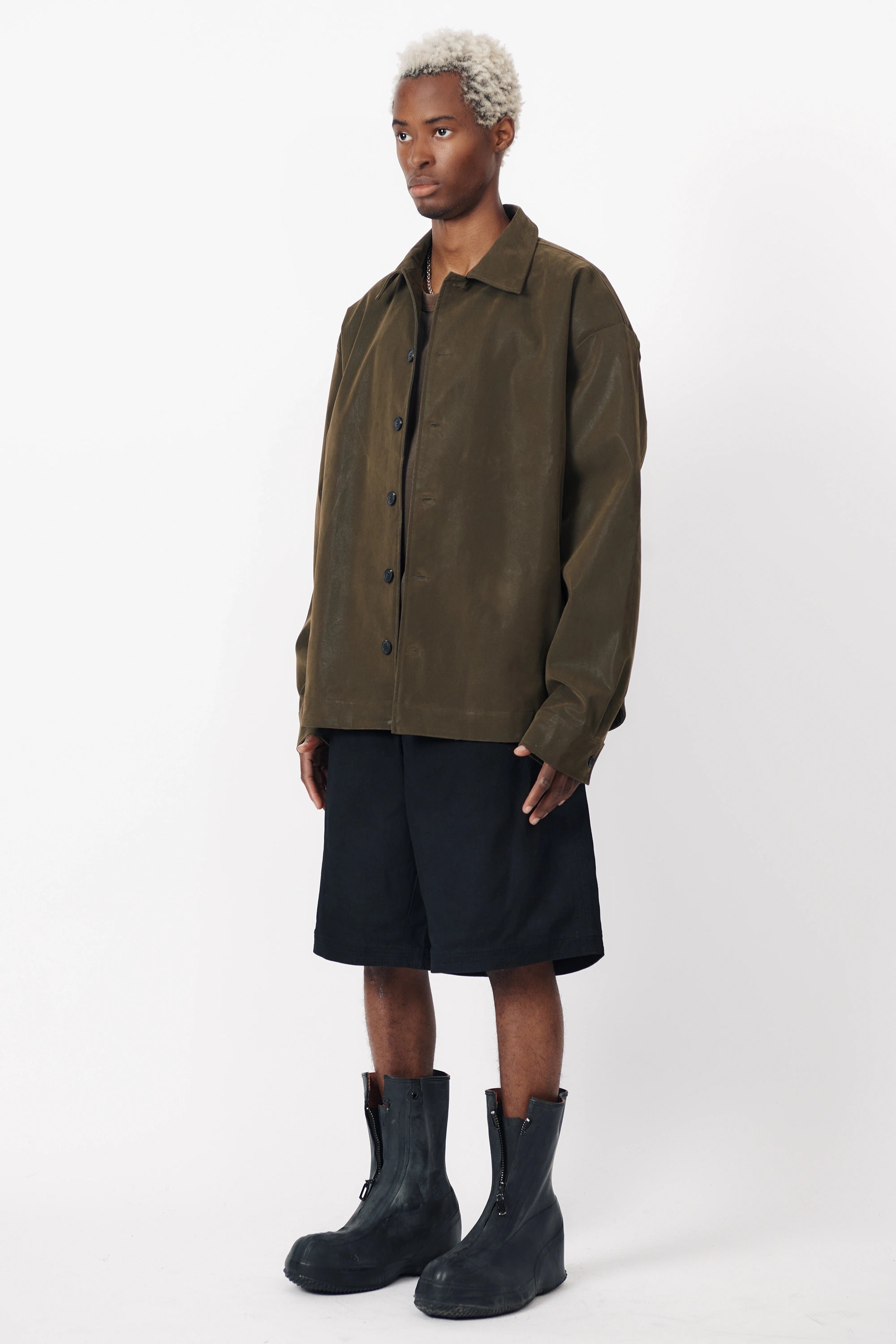 A person standing facing off to the side wearing the Beach Brains black baggy shorts an oversized green shirt with front pleats.