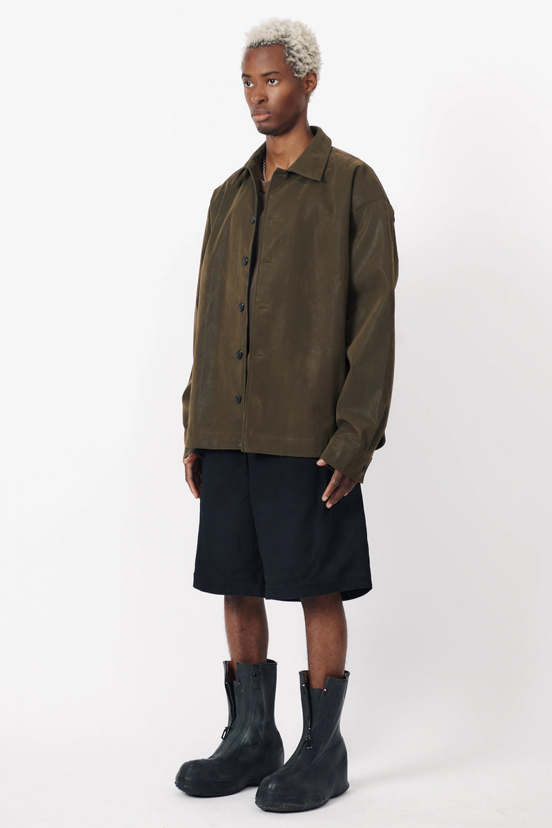 A person standing facing off to the side wearing the Beach Brains black baggy shorts an oversized green shirt with front pleats.
