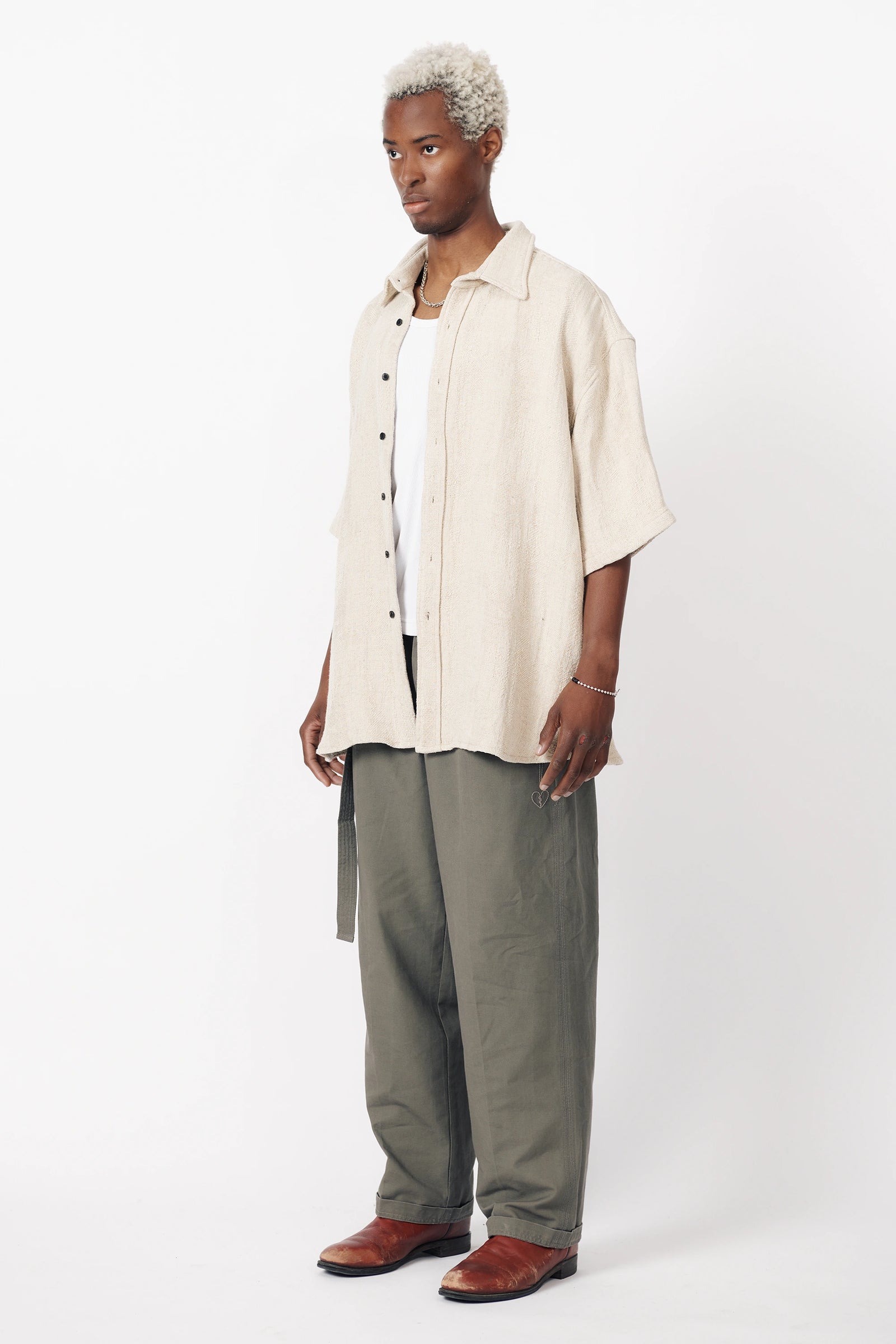 View from the side of a man wearing an oversized white short-sleeved shirt with a collar, paired with dark trousers.