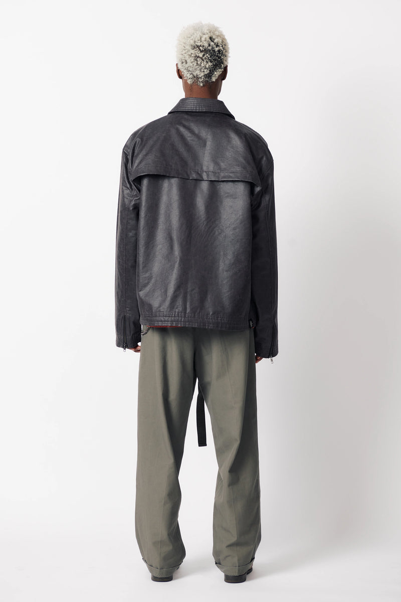 A male model with his back turned wearing a dark stone coloured coach jacket paired with grey trousers and standing against a white background
