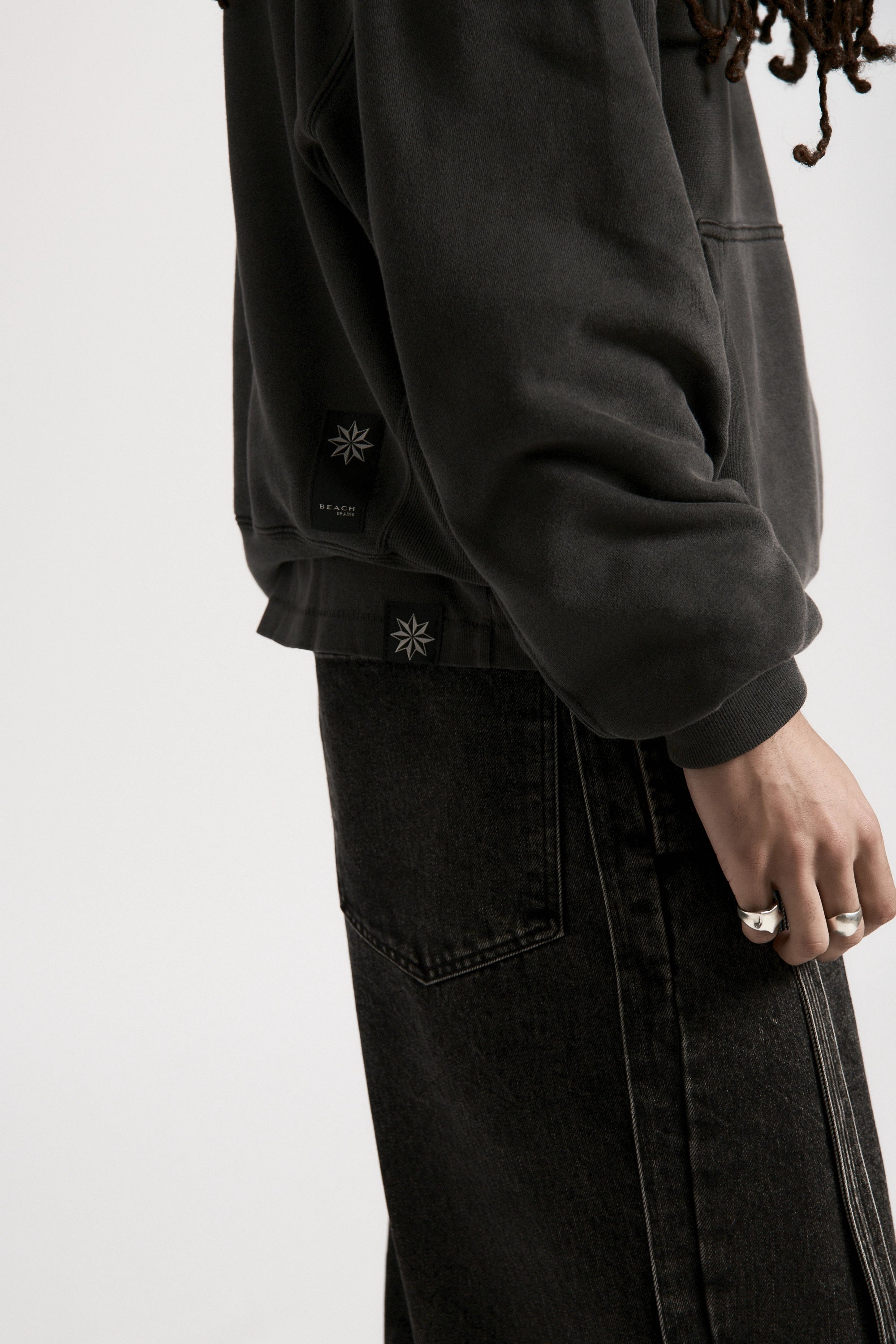 View from the side of a person wearing a dark boxy hoodie with front kangaroo pockets paired with black trousers
