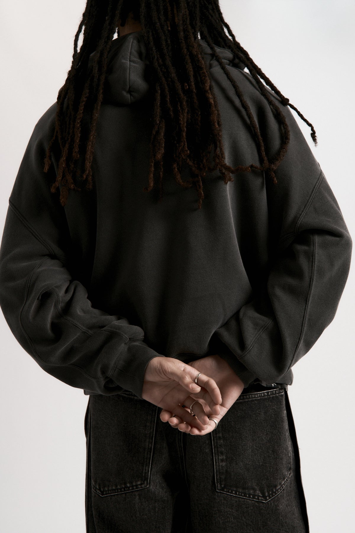 View form behind of a person wearing a dark hoodie and pants on a white background