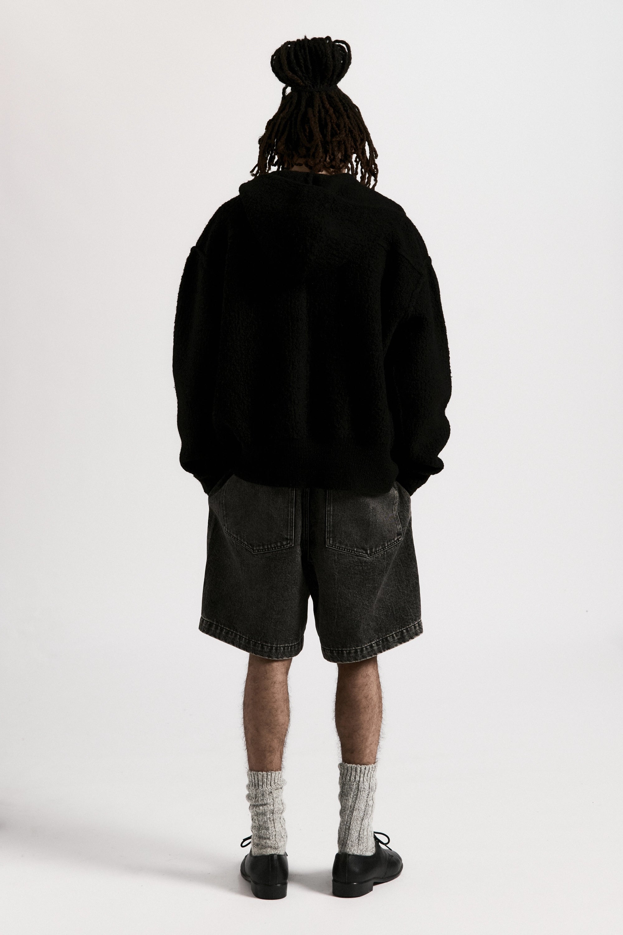 Person wearing a black jacket and washed black denim shorts with a white background