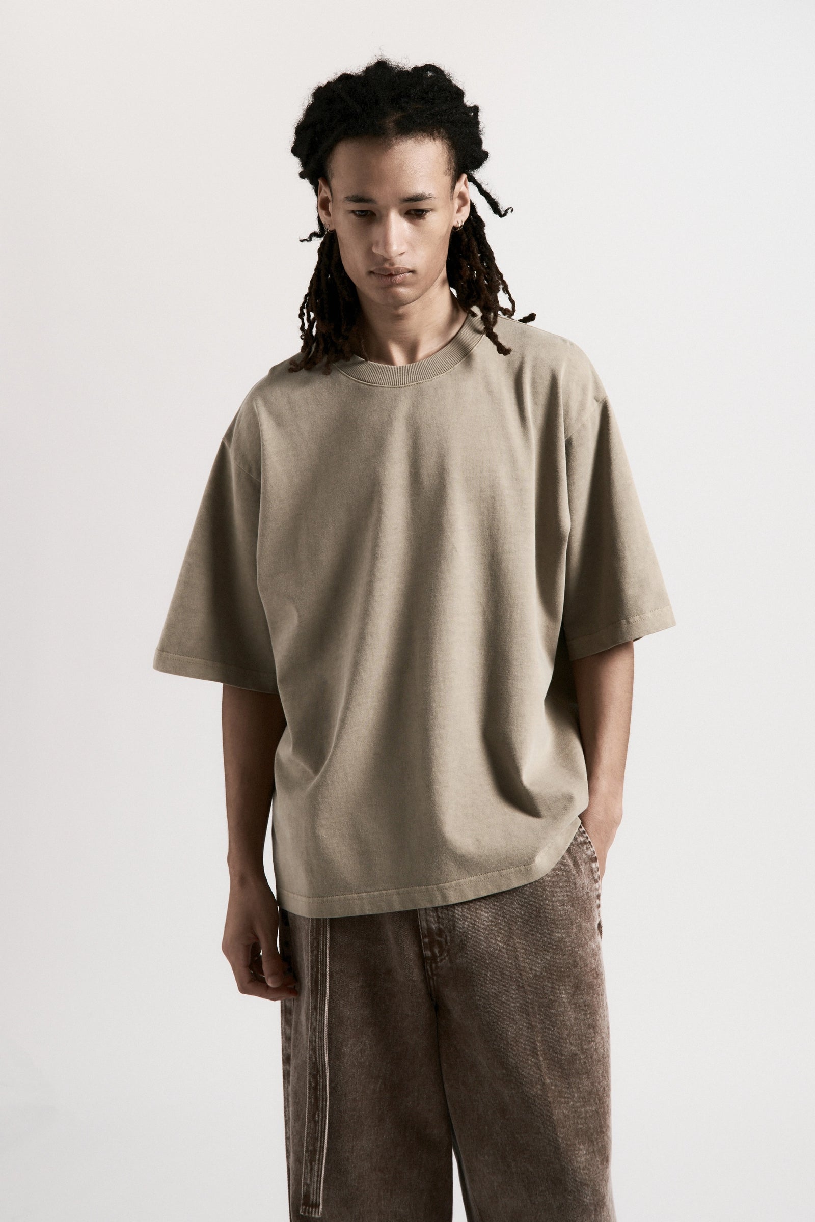 Person wearing a beige t-shirt and brown pants on a white background