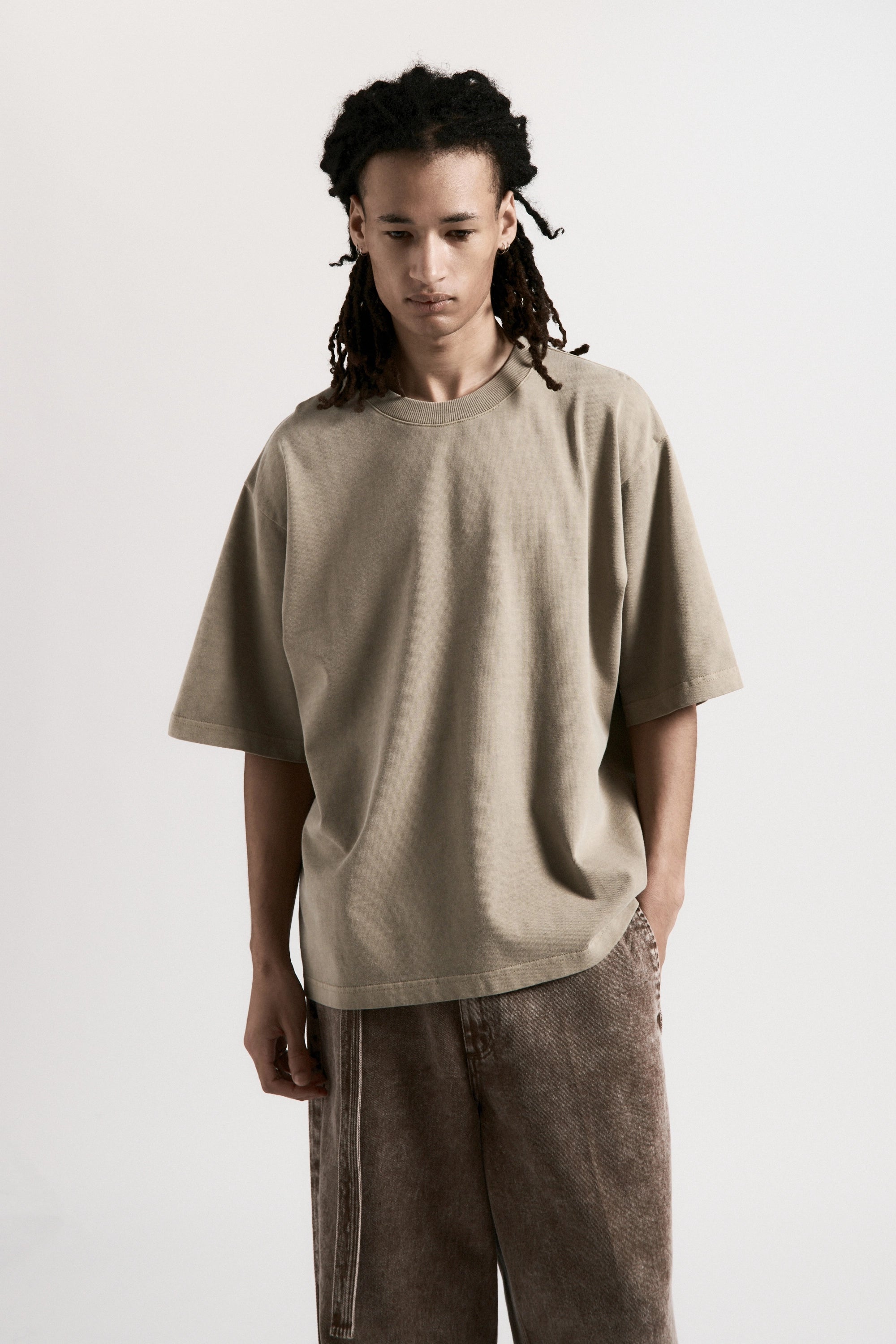 Person wearing a beige t-shirt and brown pants on a white background