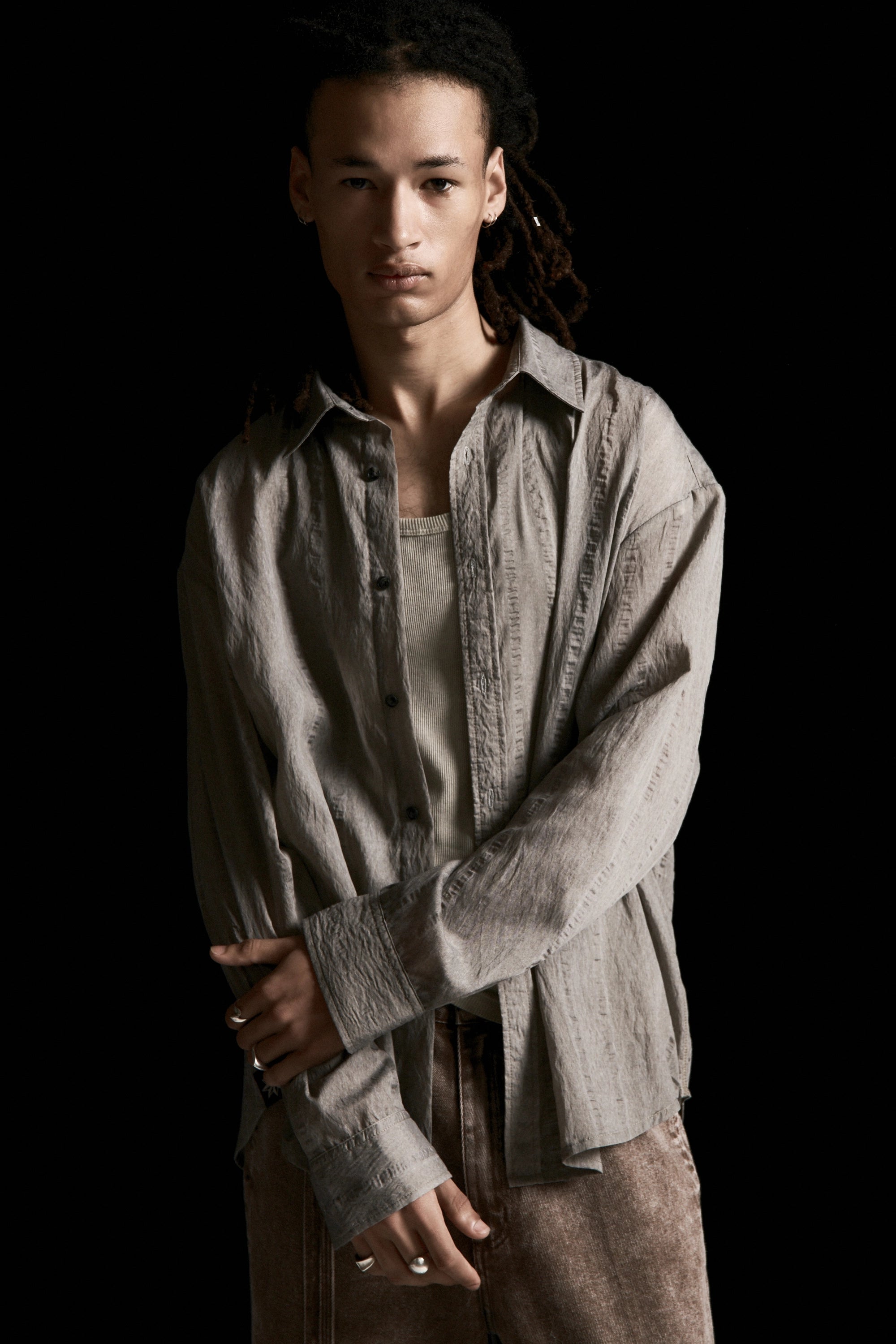 Person wearing a Sheer Grey Drop Long Sleeve Shirt over a beige tank top with a black background