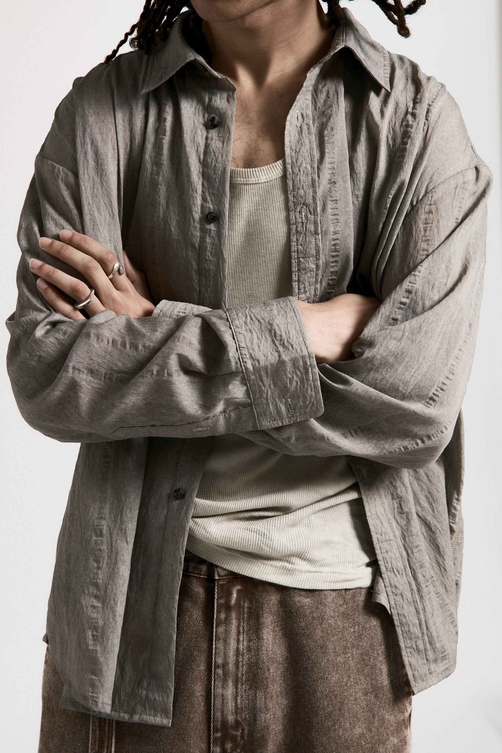 Person wearing a grey shirt over a white tank top with rolled-up sleeves, standing against a plain background.
