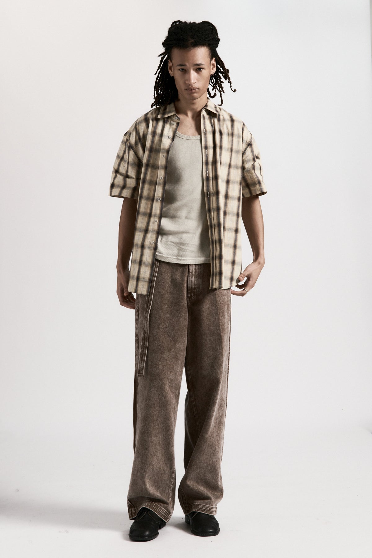 Person wearing a Cream Plaid Drop Short Sleeve Shirt, grey tank top and brown pants on a white background