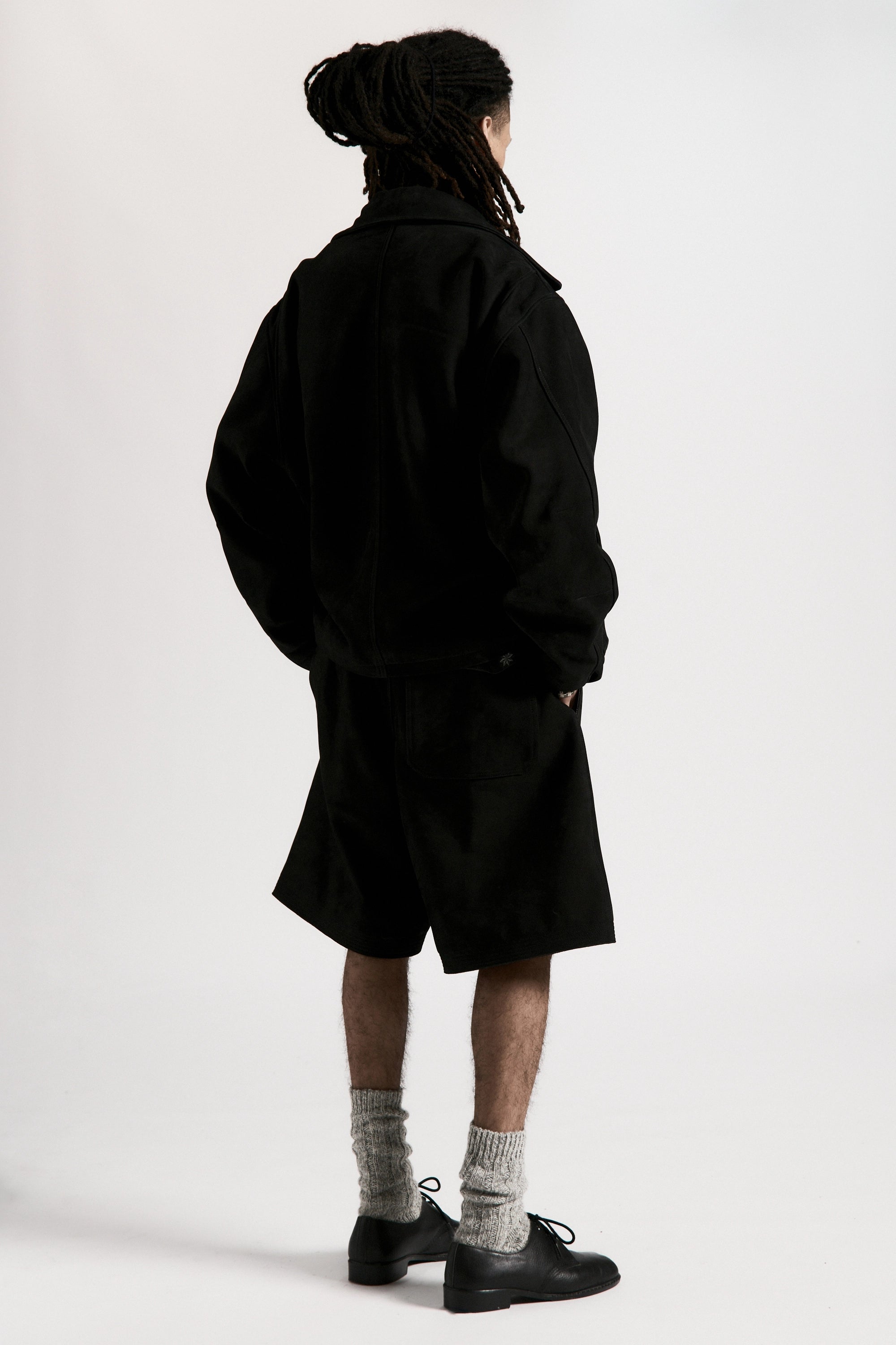 View from behind of a person wearing a black shirt and black hang shorts on a white background