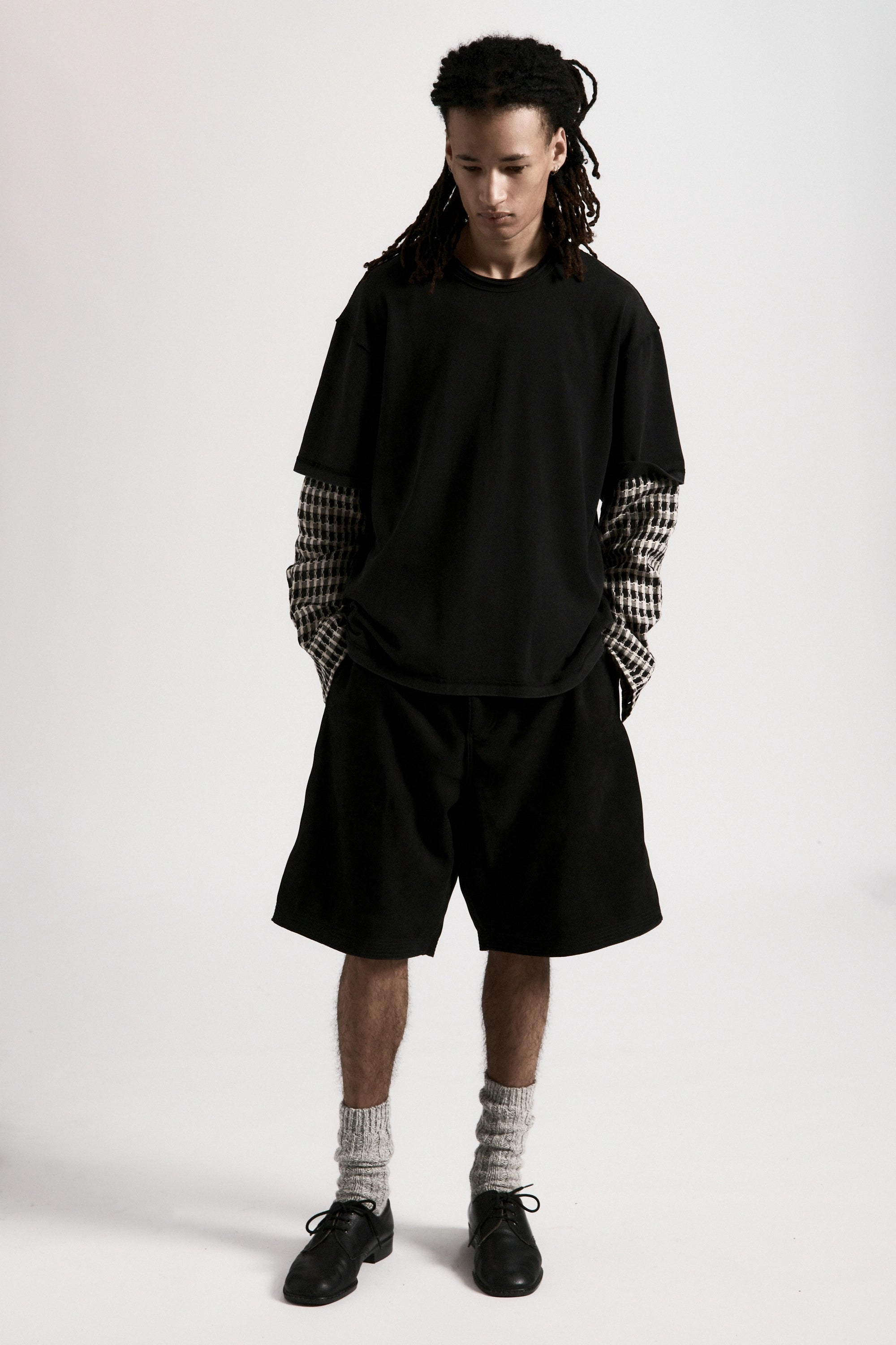 Person wearing a black shirt with checkered sleeves and black hang shorts on a white background