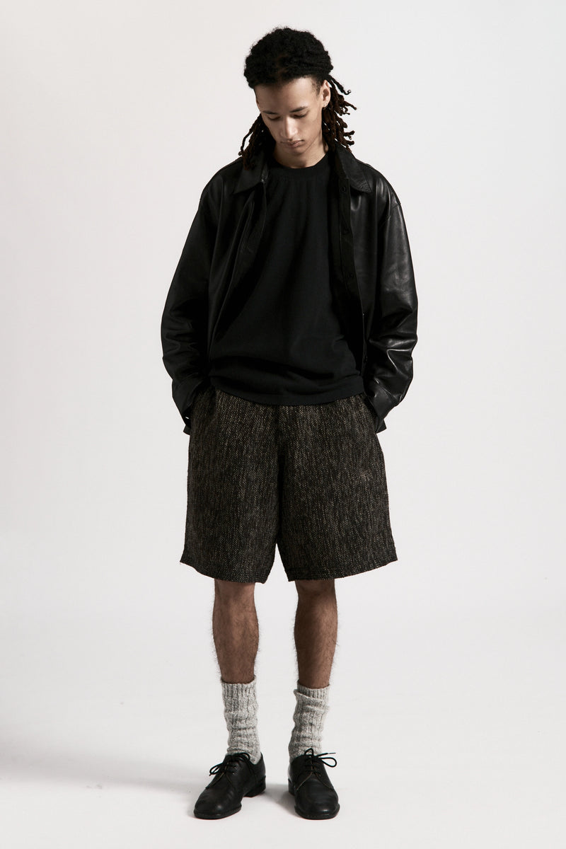 Person wearing a black leather jacket, black shirt and grey fossil hang shorts on a white background