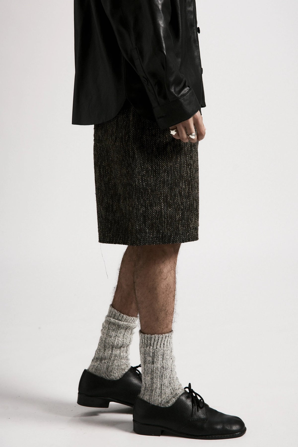 Person wearing a dark jackte, grey fossil hang shorts and black shoes with white socks on a plain background