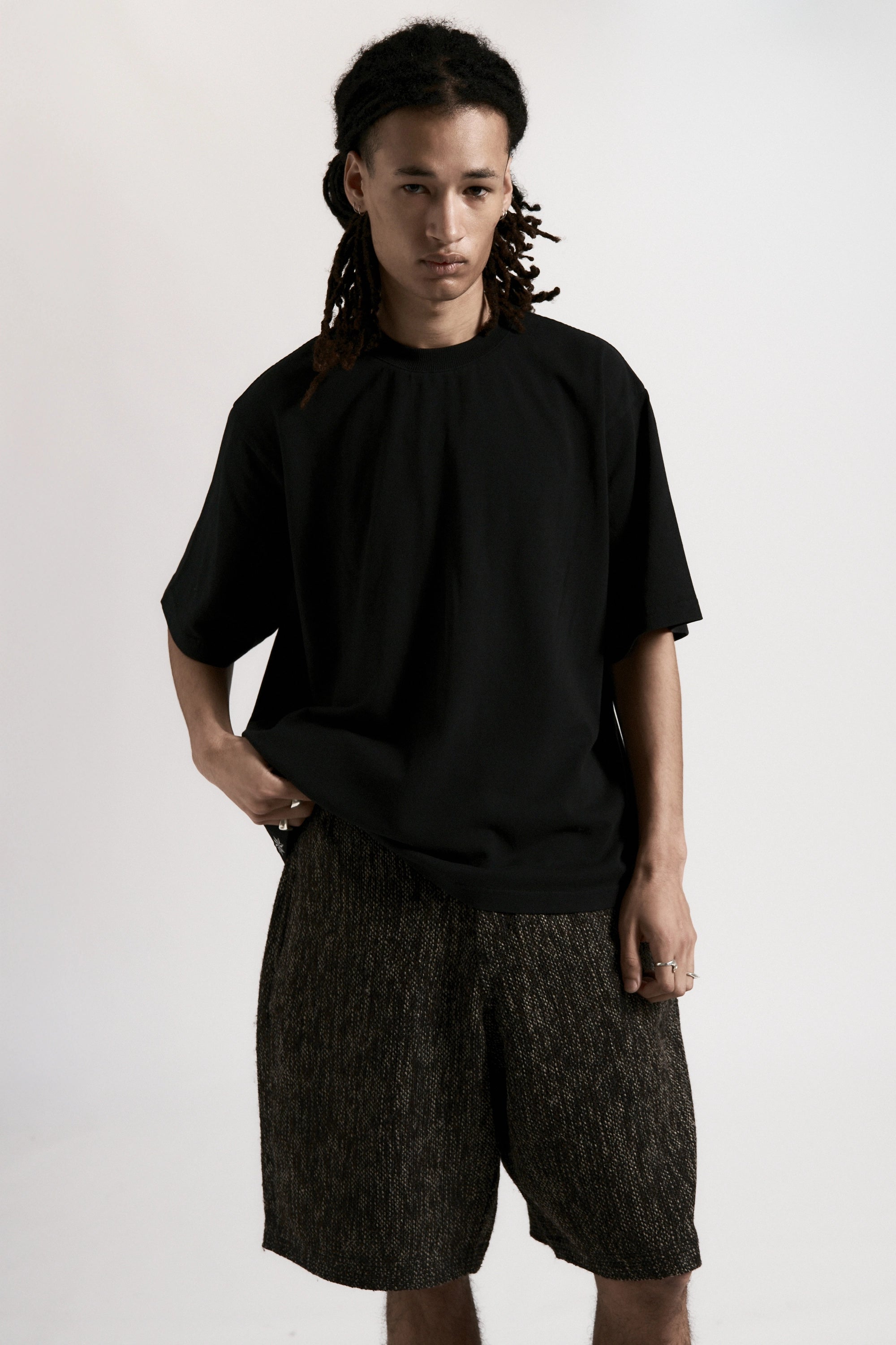 Person wearing a black t-shirt and grey patterned shorts on a white background