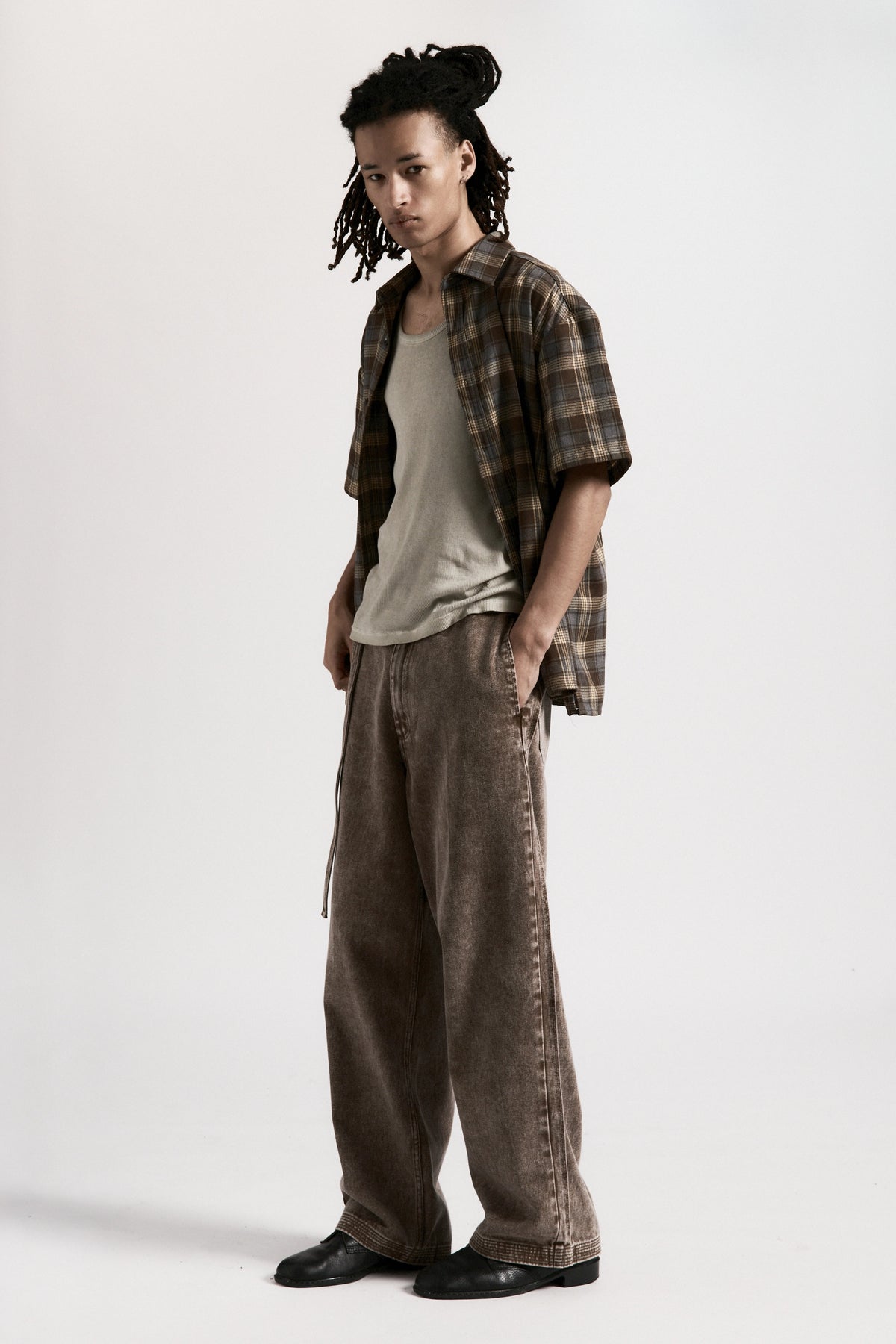 Person wearing a plaid shirt, white t-shirt, and brown pants on a white background