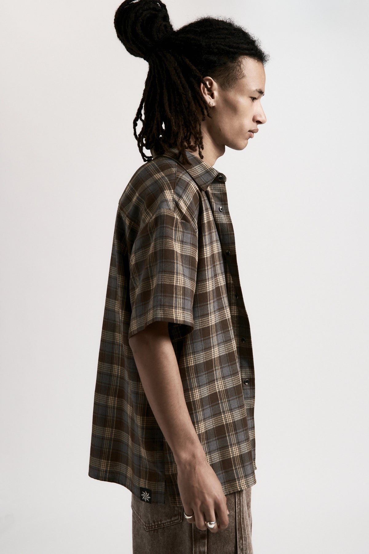 Person facing to the side wearing a Brown & Blue Hold Short Sleeve Shirt on a light grey background
