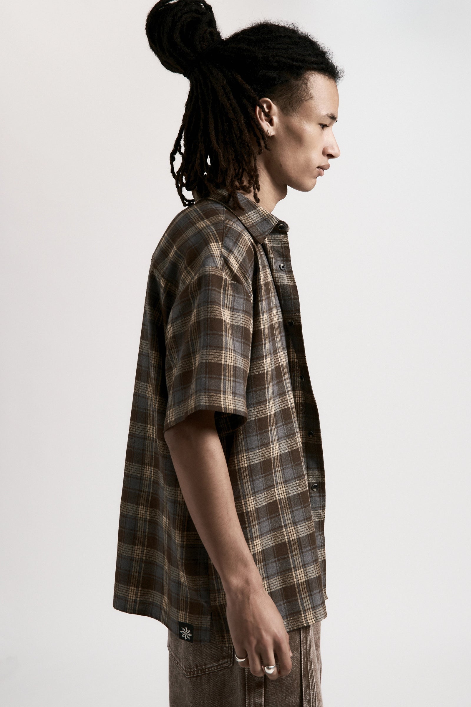 Person facing to the side wearing a Brown & Blue Hold Short Sleeve Shirt on a light grey background
