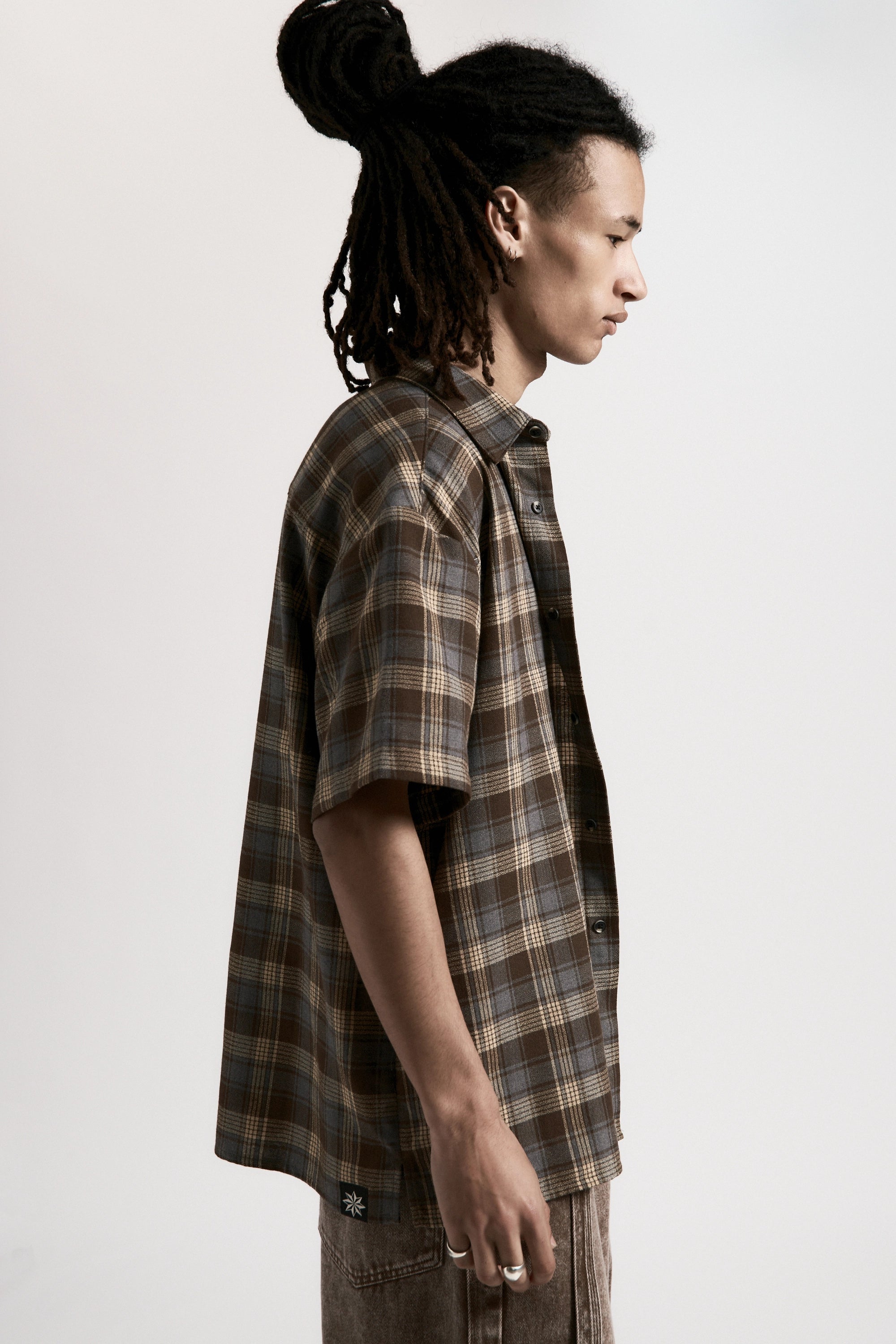 Person facing to the side wearing a Brown & Blue Hold Short Sleeve Shirt on a light grey background