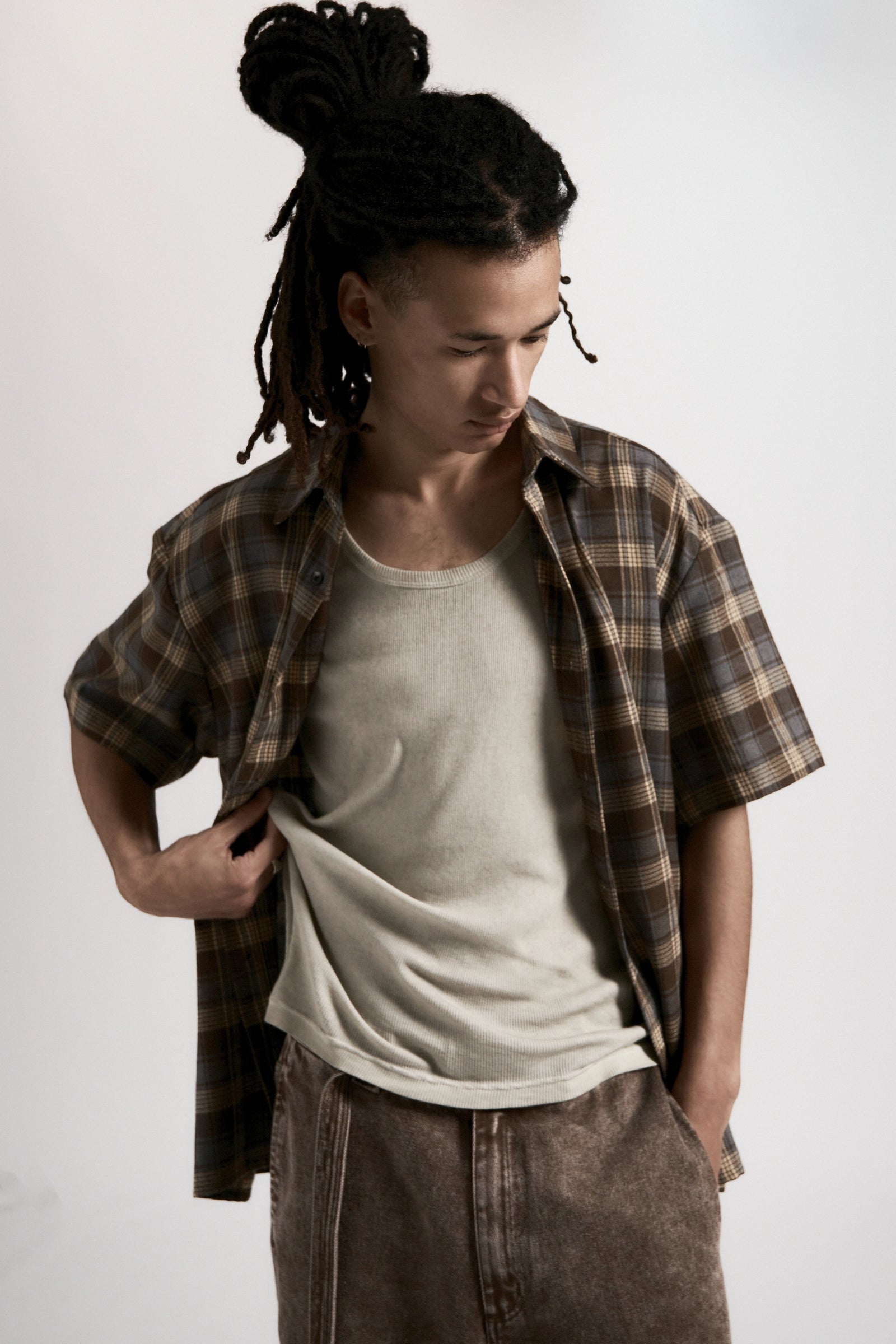 Person wearing a plaid shirt over a white t-shirt with brown pants on a plain background