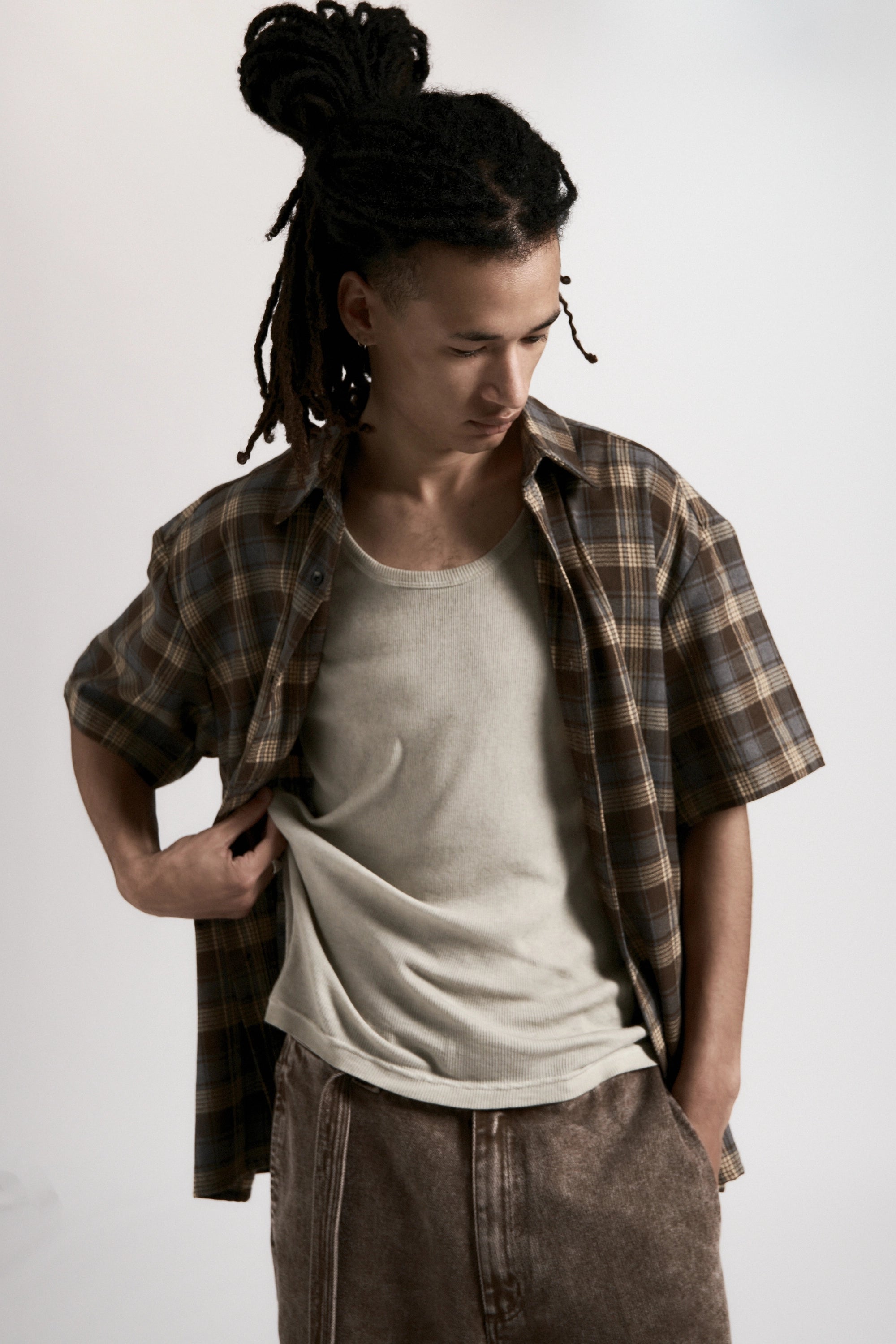 Person wearing a plaid shirt over a white t-shirt with brown pants on a plain background