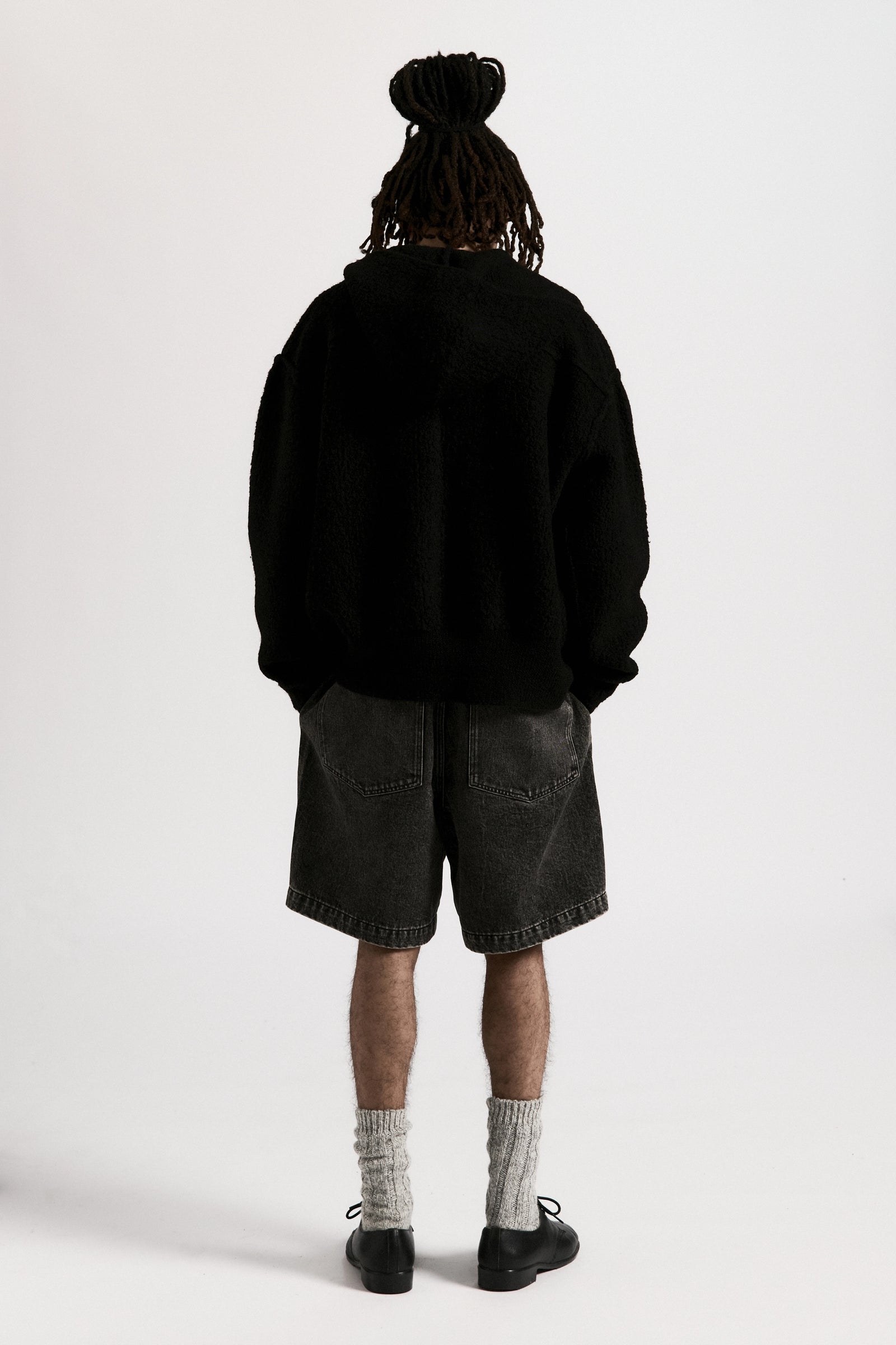 View from behind of a person wearing a black boiled wool knit zipped hoodie and shorts on a white background