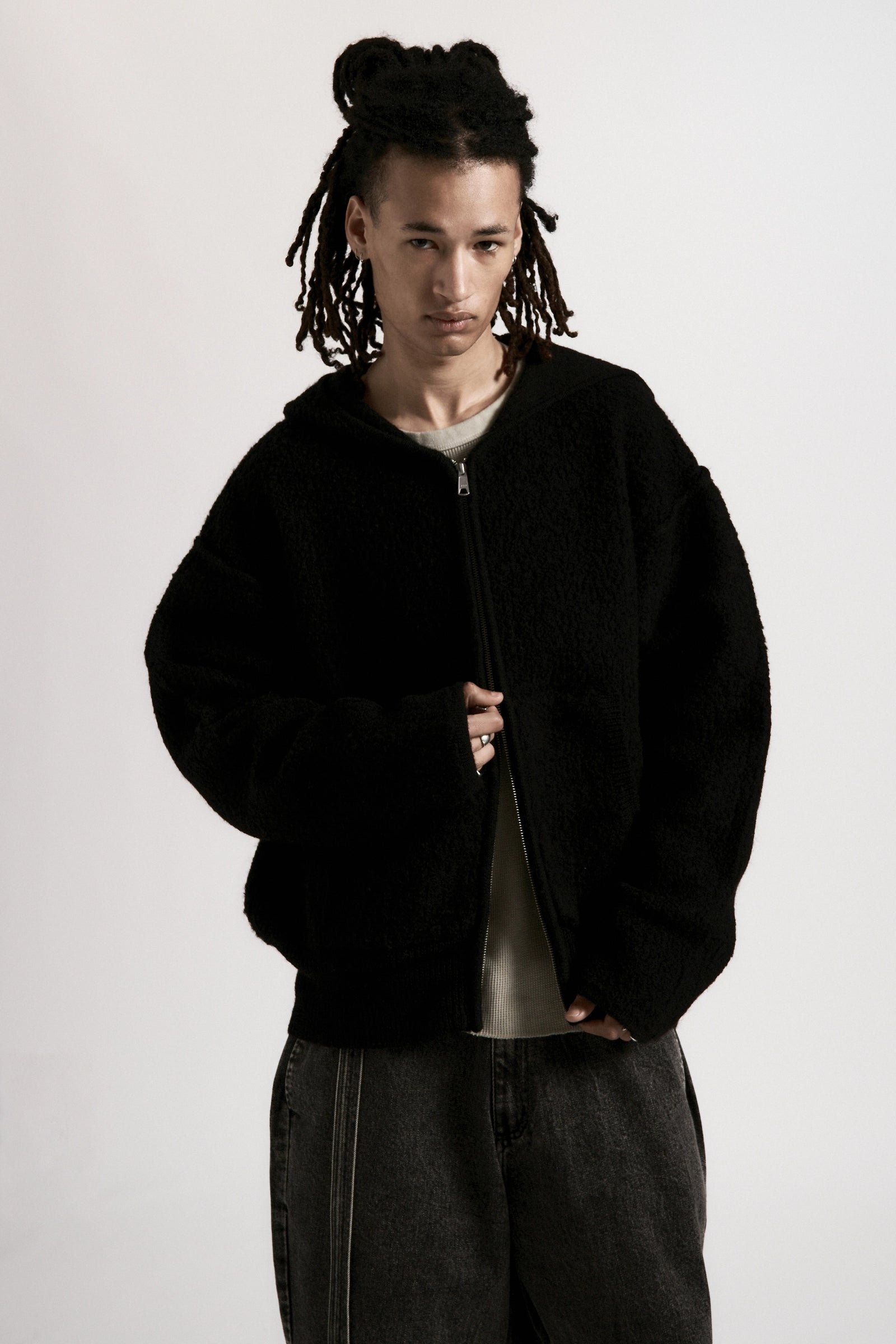 A male model wearing a black zipped hoodie on a white background