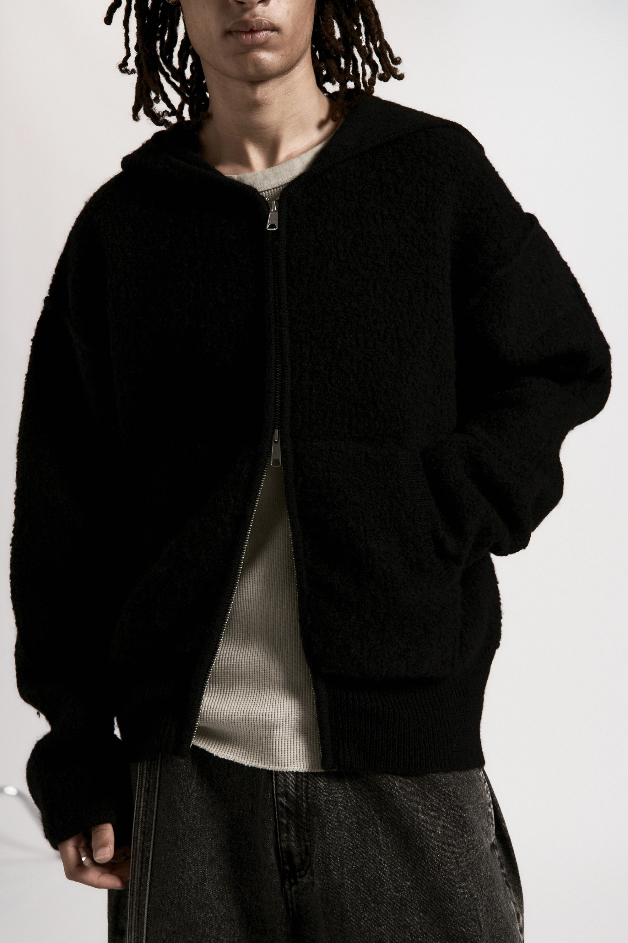 Person wearing a black boiled wool zipped hoodie over a white shirt on a plain background