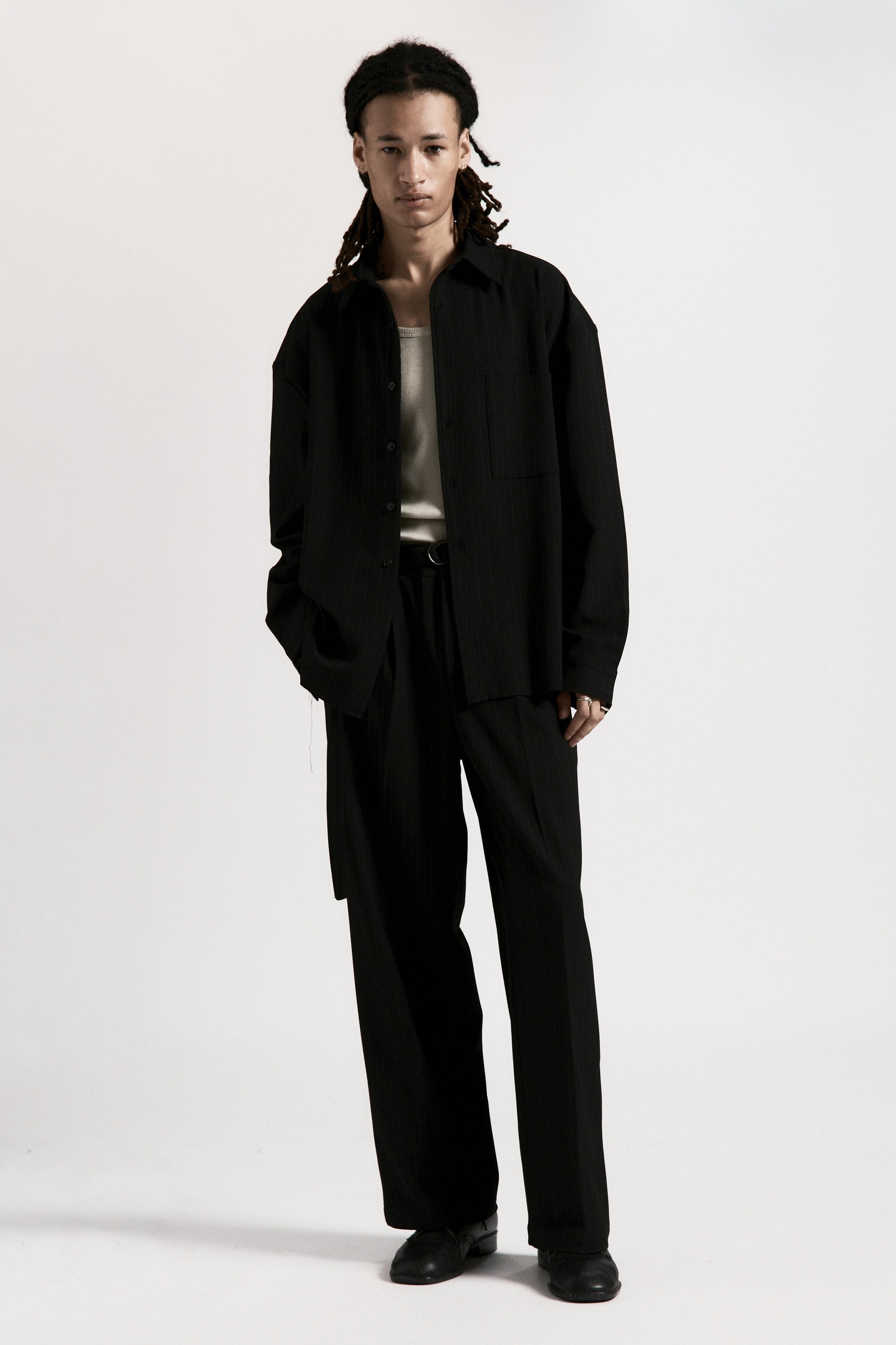 Person wearing a jacket over a white top with black pants and dark shoes on a white background