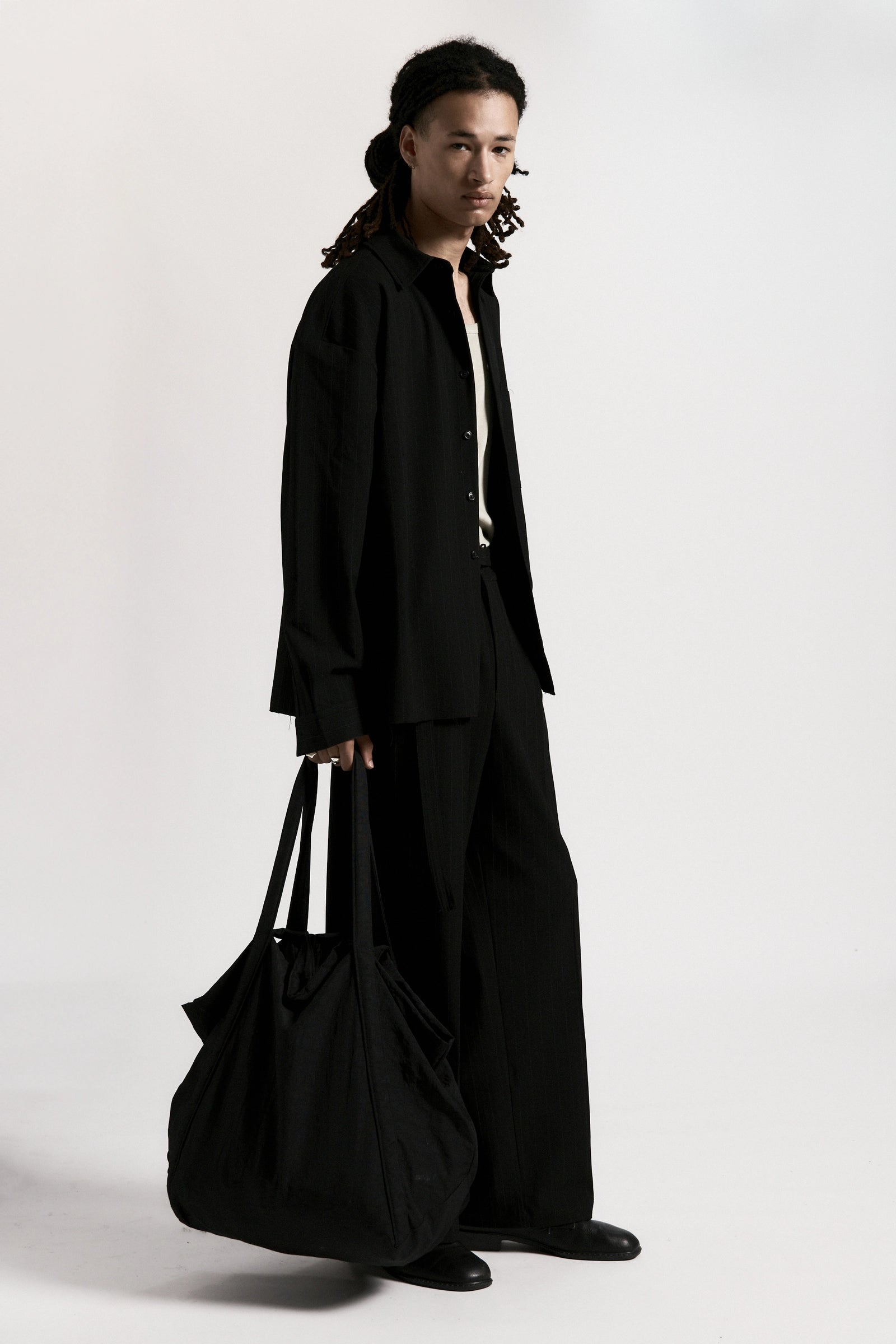 Person wearing a black suit holding a black bag on a white background