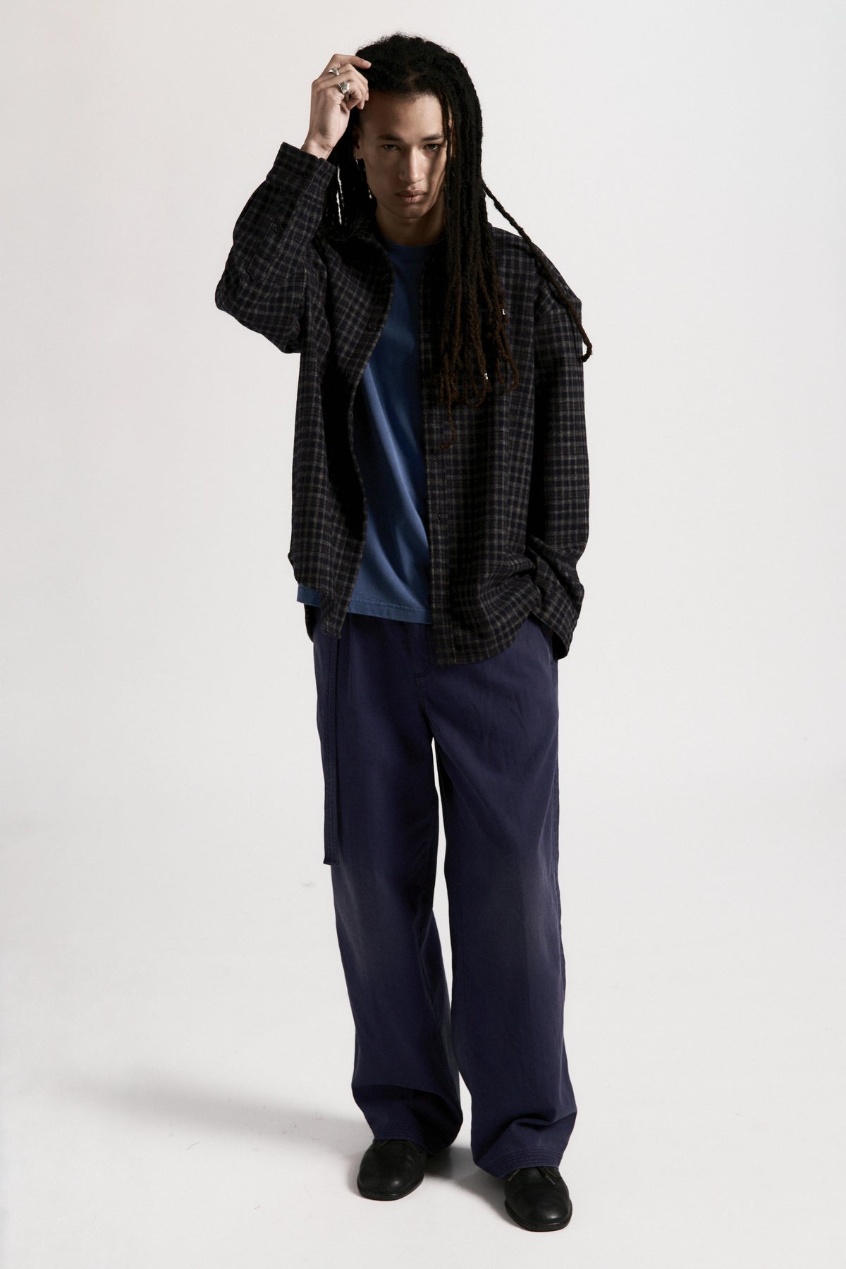 Person wearing a plaid shirt over a blue top with navy blue pleated work pants on a white background