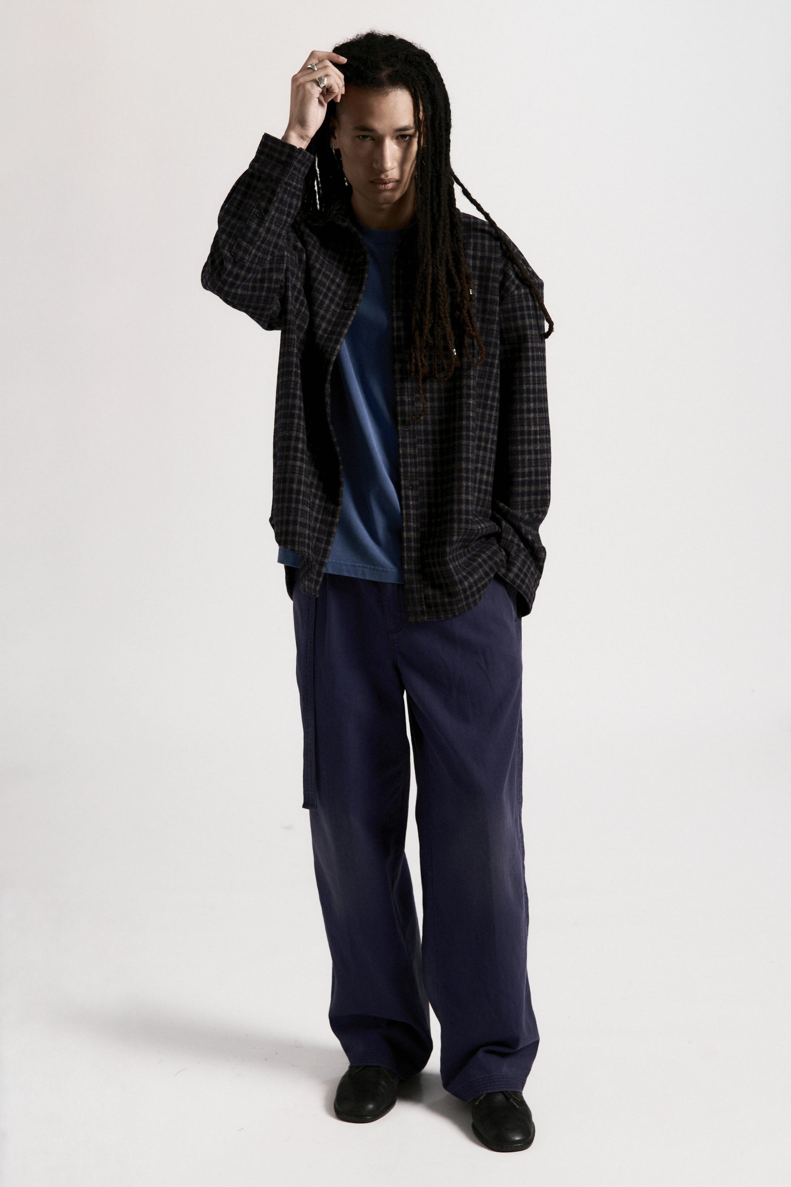 Person wearing a plaid shirt over a blue top with navy blue pleated work pants on a white background