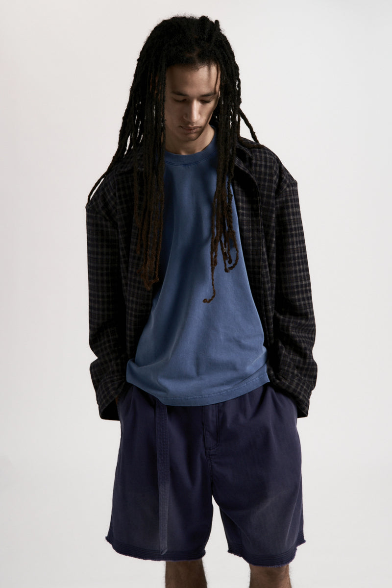 Person wearing a blue shirt and dark shorts with a plaid jacket on a white background