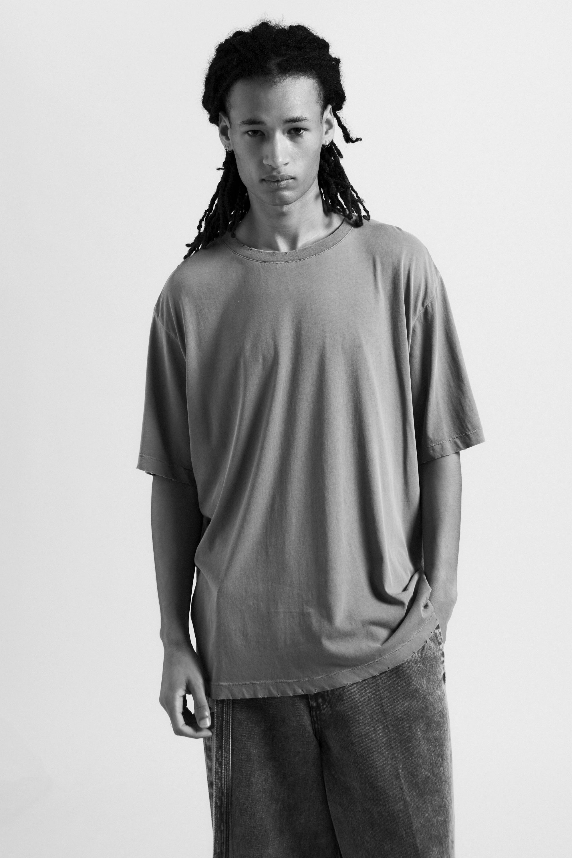 Person wearing a plain grey oversied t-shirt and dark pants on a light background