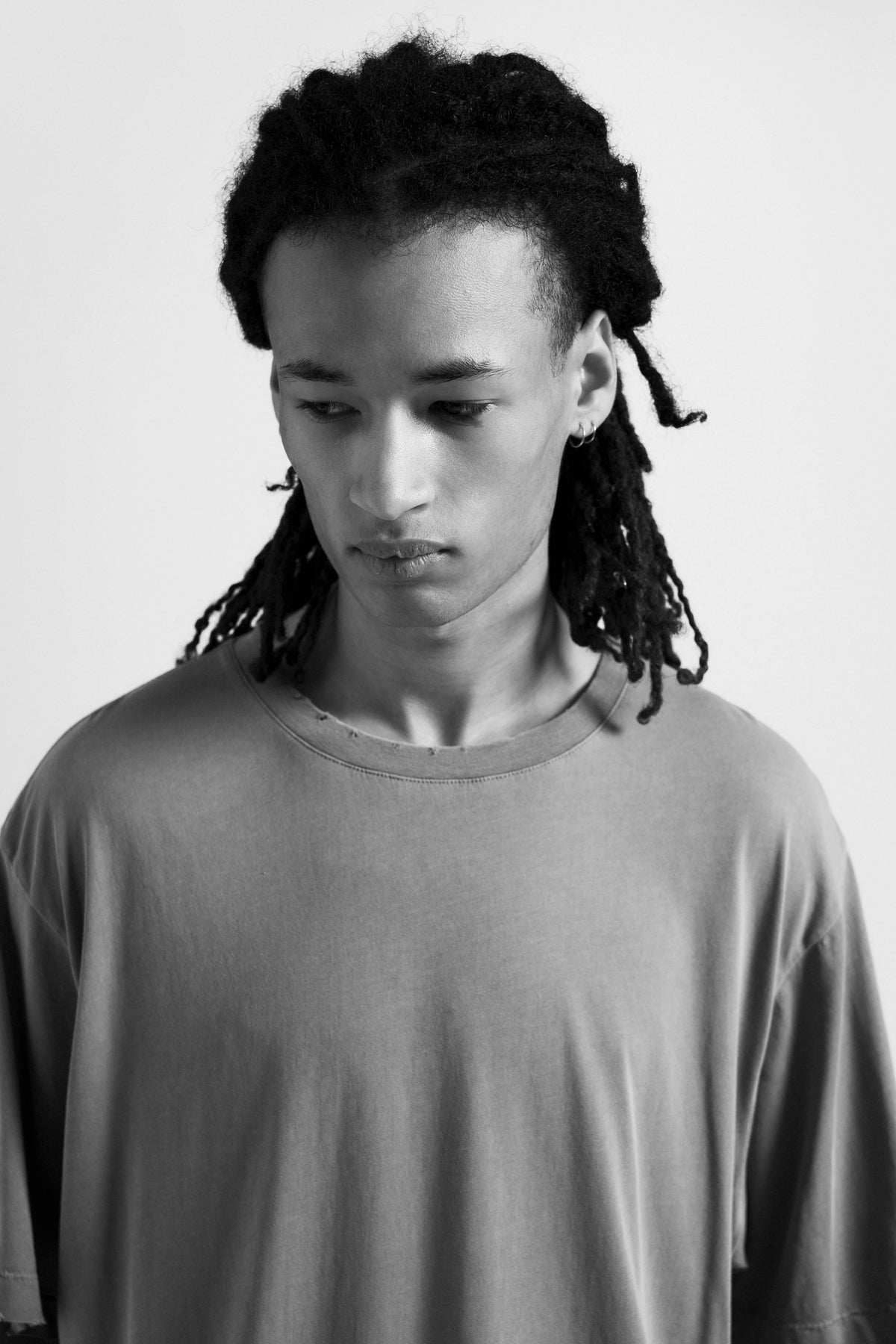 Black and white portrait of a person with braided hair wearing a plain grey oversized shirt.