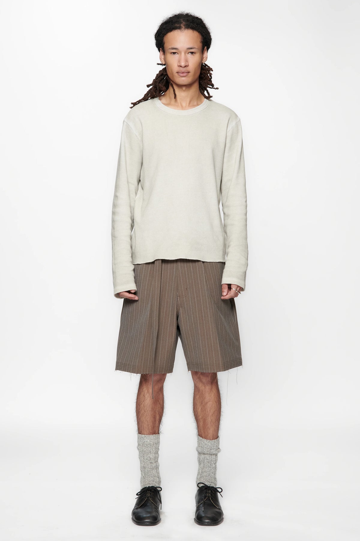 Person wearing a light-coloured sweater and brown pinstripe cut shorts on a white background