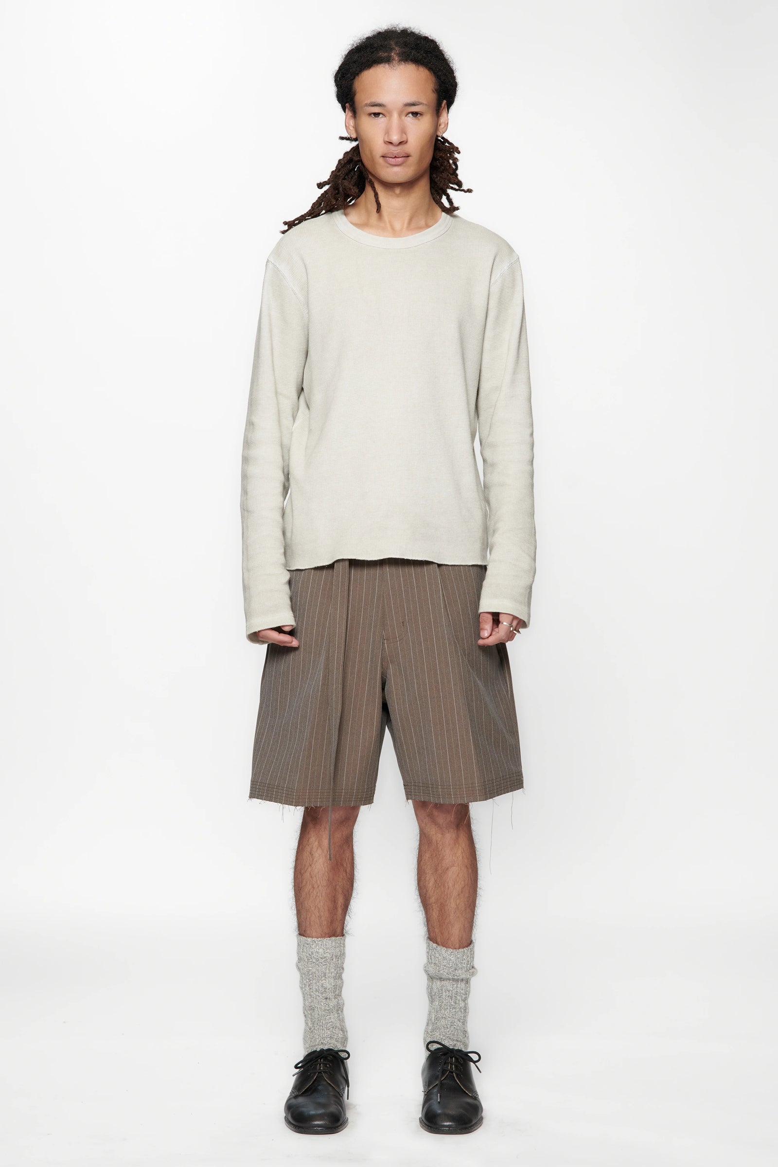 Person wearing a light-coloured sweater and brown pinstripe cut shorts on a white background