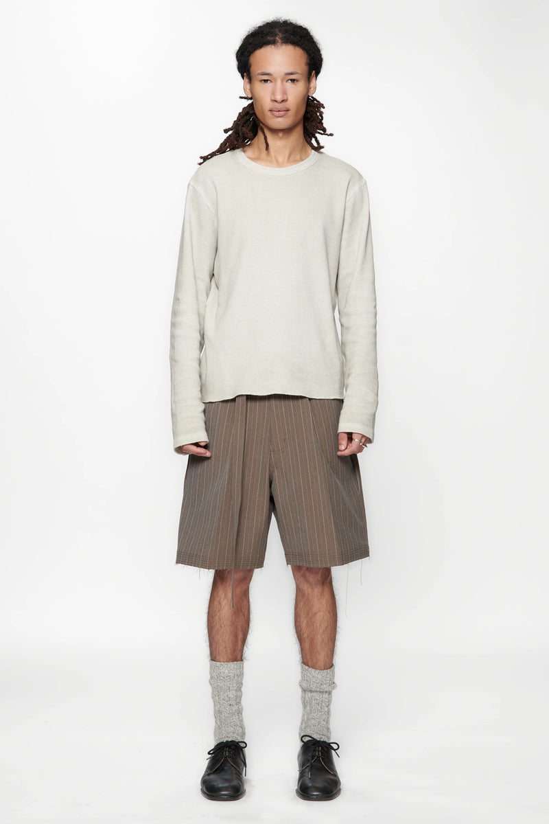 Person wearing a light-coloured sweater and brown pinstripe cut shorts on a white background
