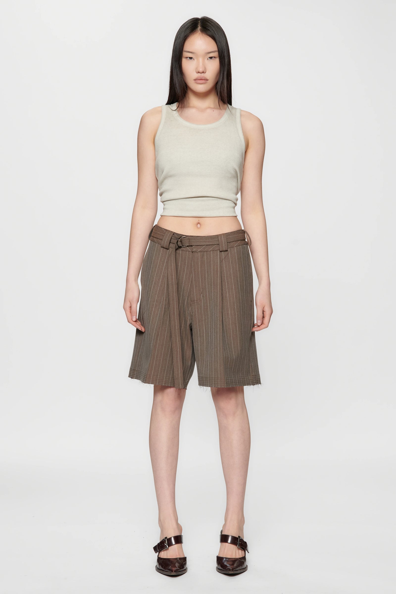 Woman wearing a light green sleeveless top and brown pinstripe cut shorts on a white background