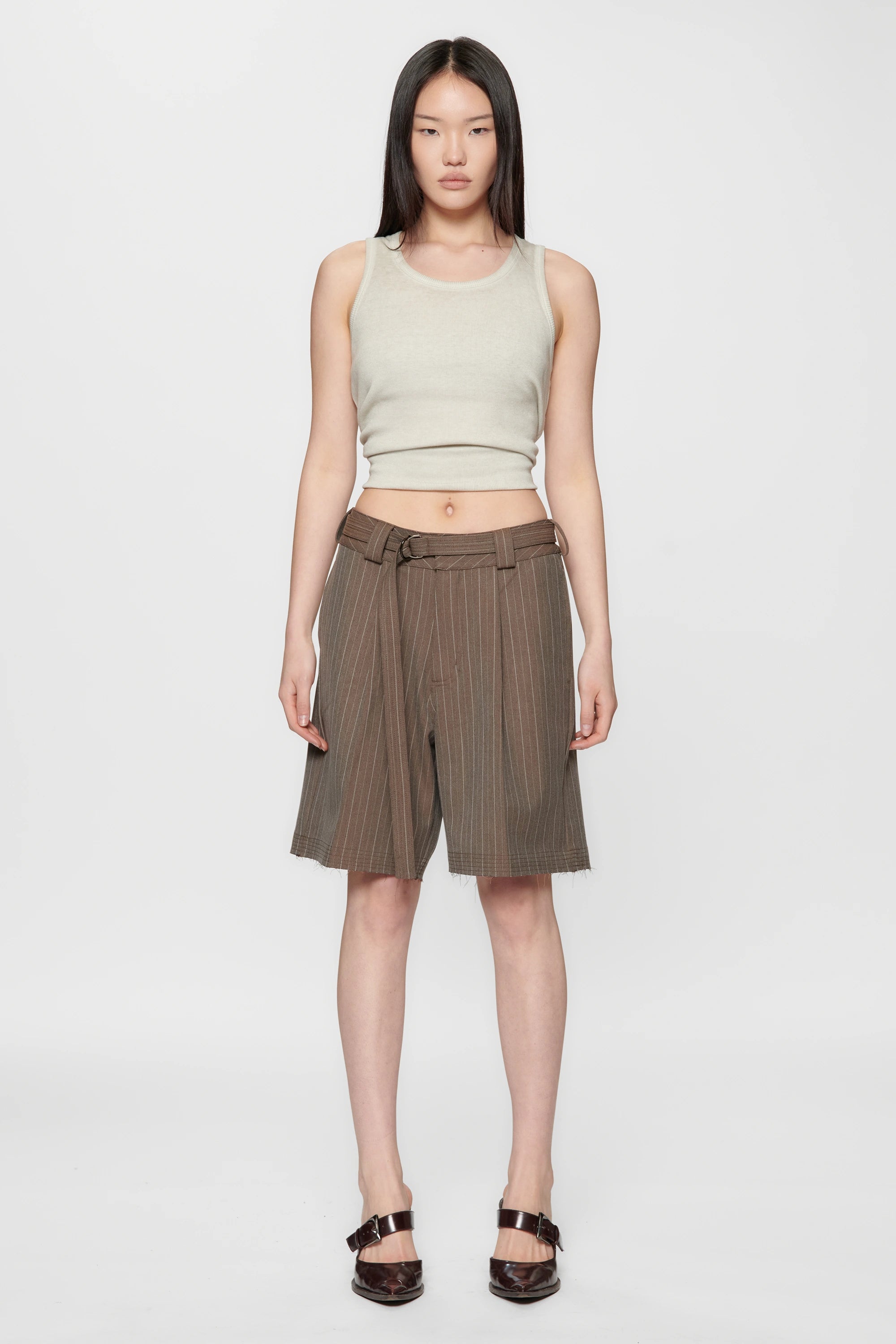 Woman wearing a light green sleeveless top and brown pinstripe cut shorts on a white background