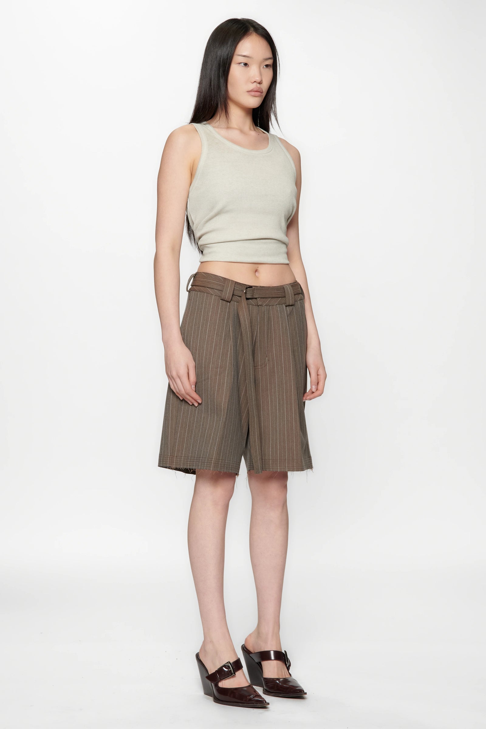 Woman wearing a light green sleeveless top and brown striped shorts on a white background