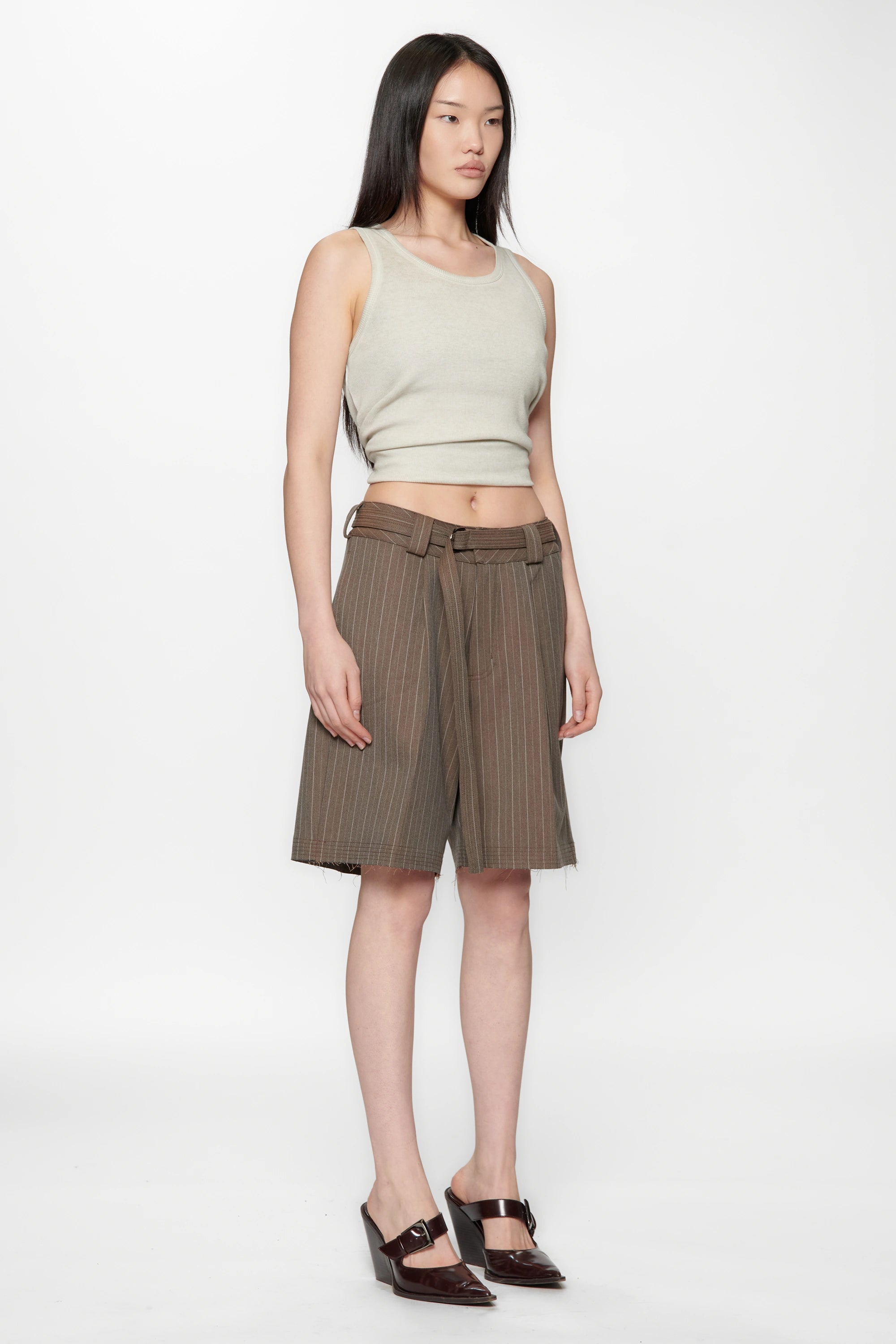 Woman wearing a light green sleeveless top and brown striped shorts on a white background