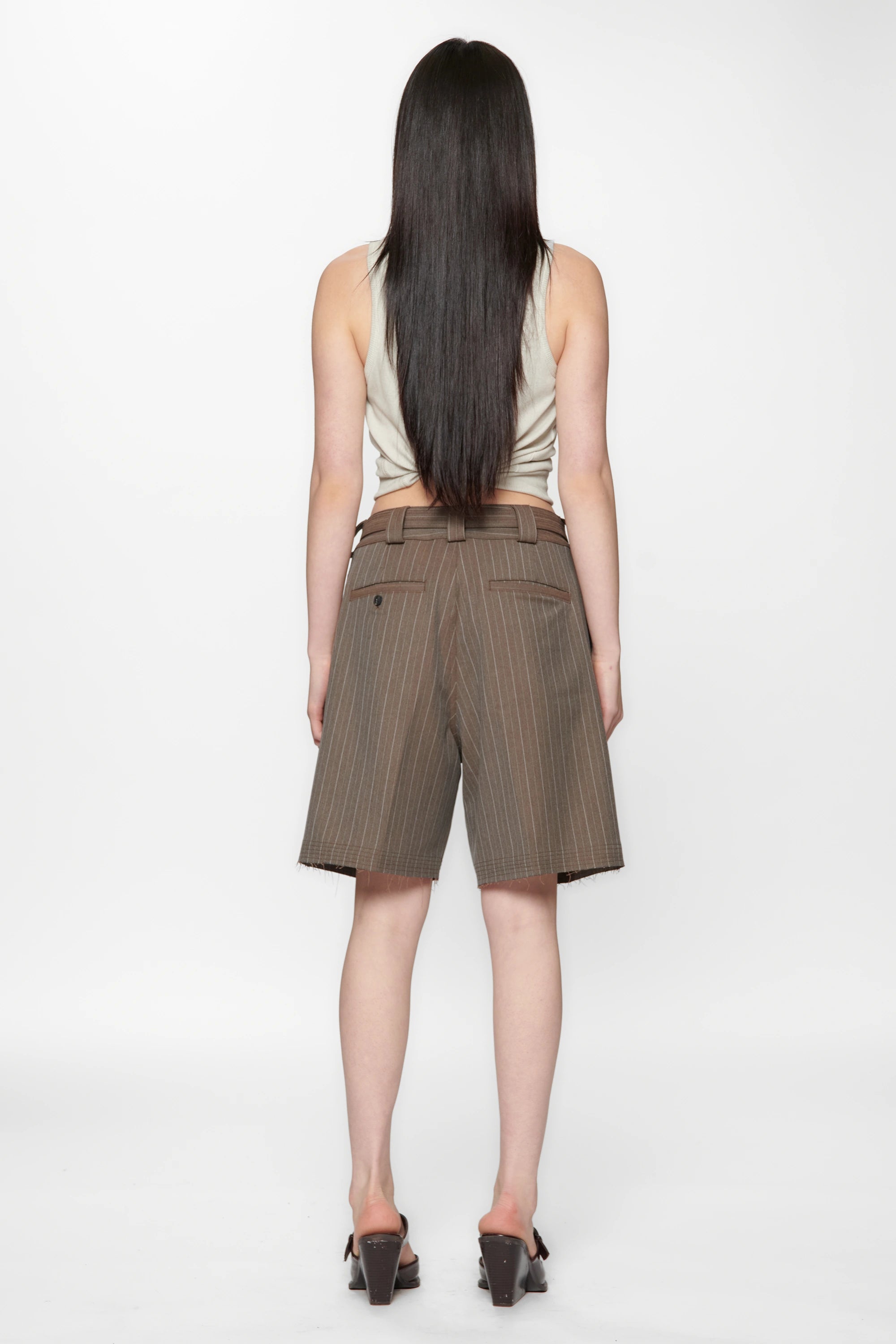 A female model with her back turned wearing brown pinstripe cut shorts on a white background