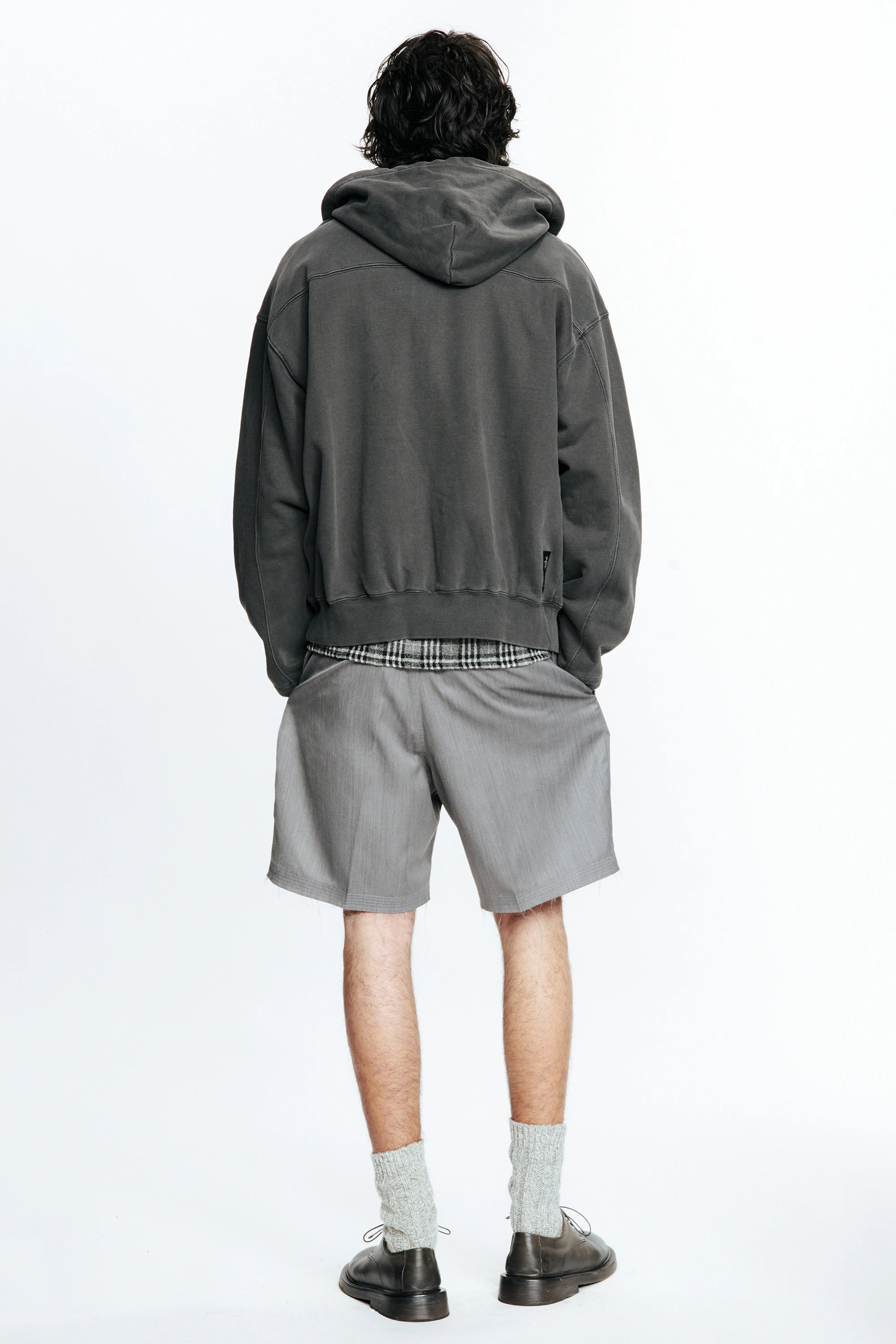 View from behind of a person wearing a grey hoodie and cut shorts on a white background